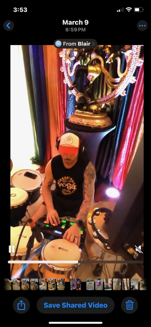A person DJing with drum sets in a colorful, decorated environment featuring a large statue of Ganesha in the background.