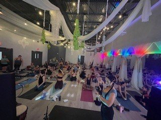 People participating in a yoga class in a decorated studio with hanging fabric and colorful lights.