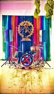 Colorful stage with rainbow curtains, a drum set, and decorative elements including a gold sculpture and green drapes.