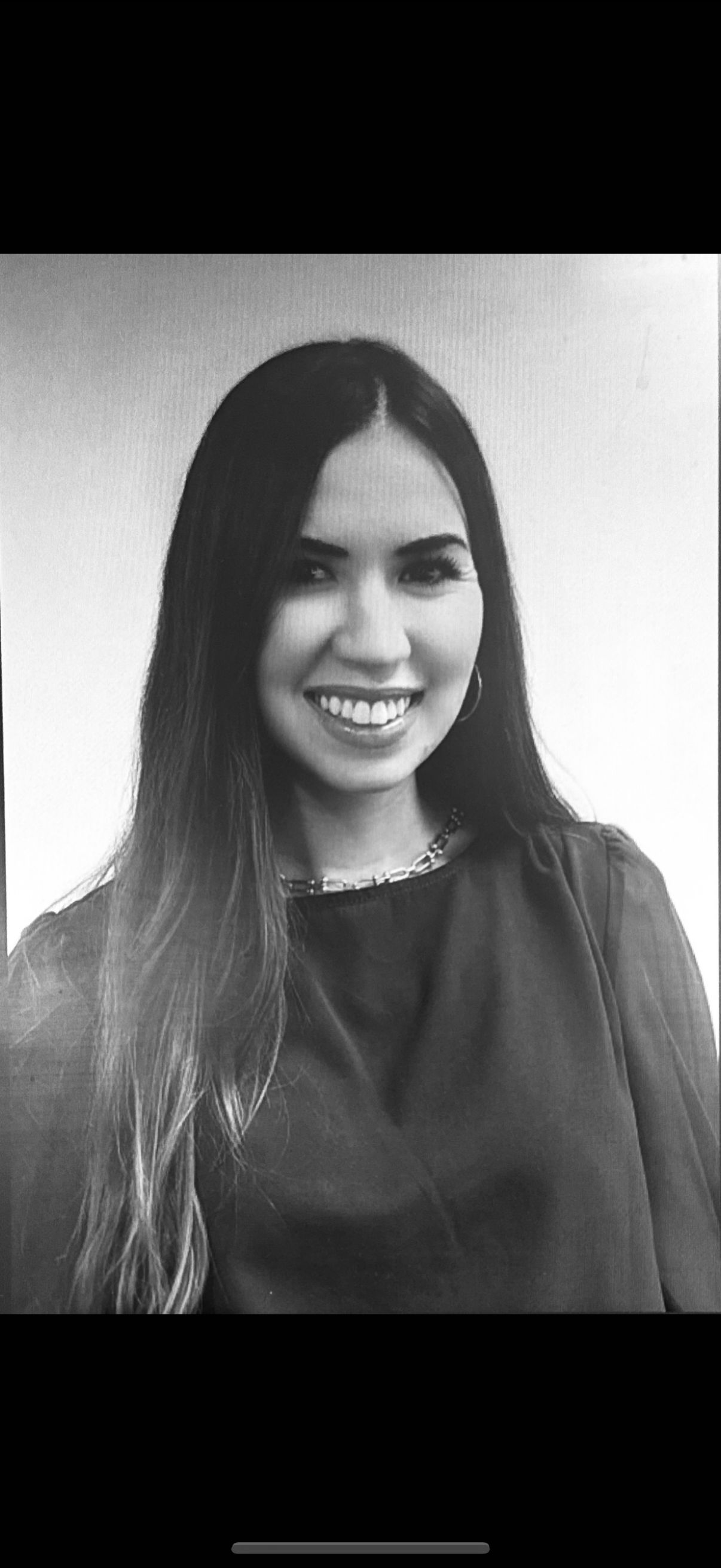 Black-and-white portrait of a smiling woman with long hair, wearing a chain necklace and hoop earrings.