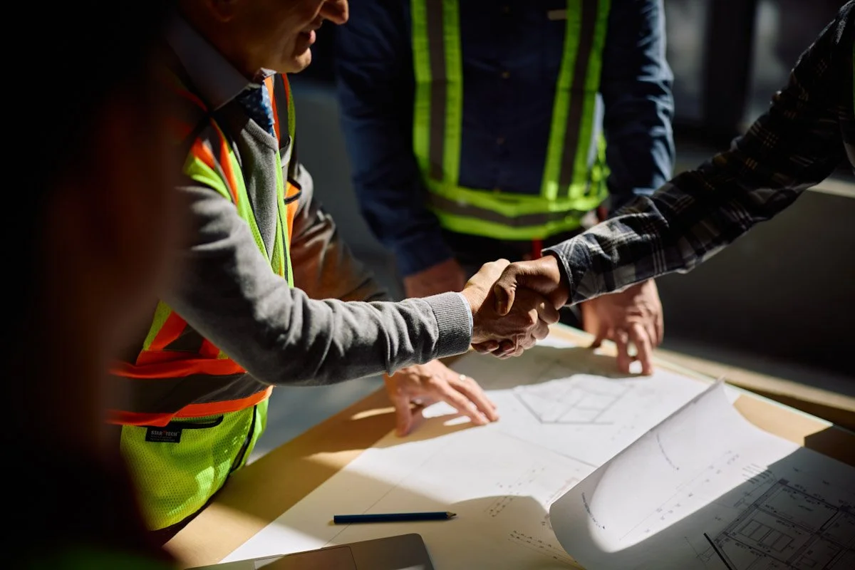 Construction worker in safety vest shaking hands with another person.