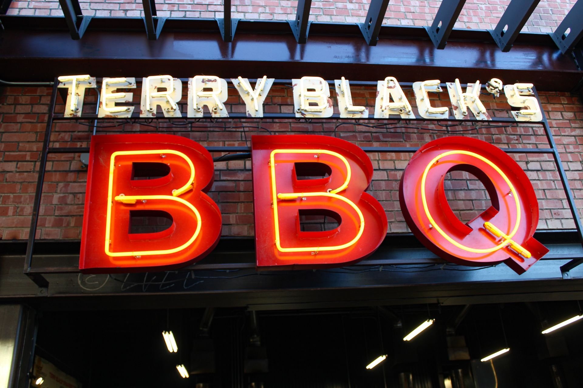 Neon sign for Terry Black's BBQ restaurant on a brick wall, with the words 'Terry Black's' in white letters and 'BBQ' in large red neon letters.