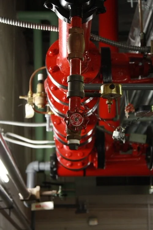 Close-up view of a red industrial sprinkler system installed on a ceiling, with pipes, valves, and fittings.