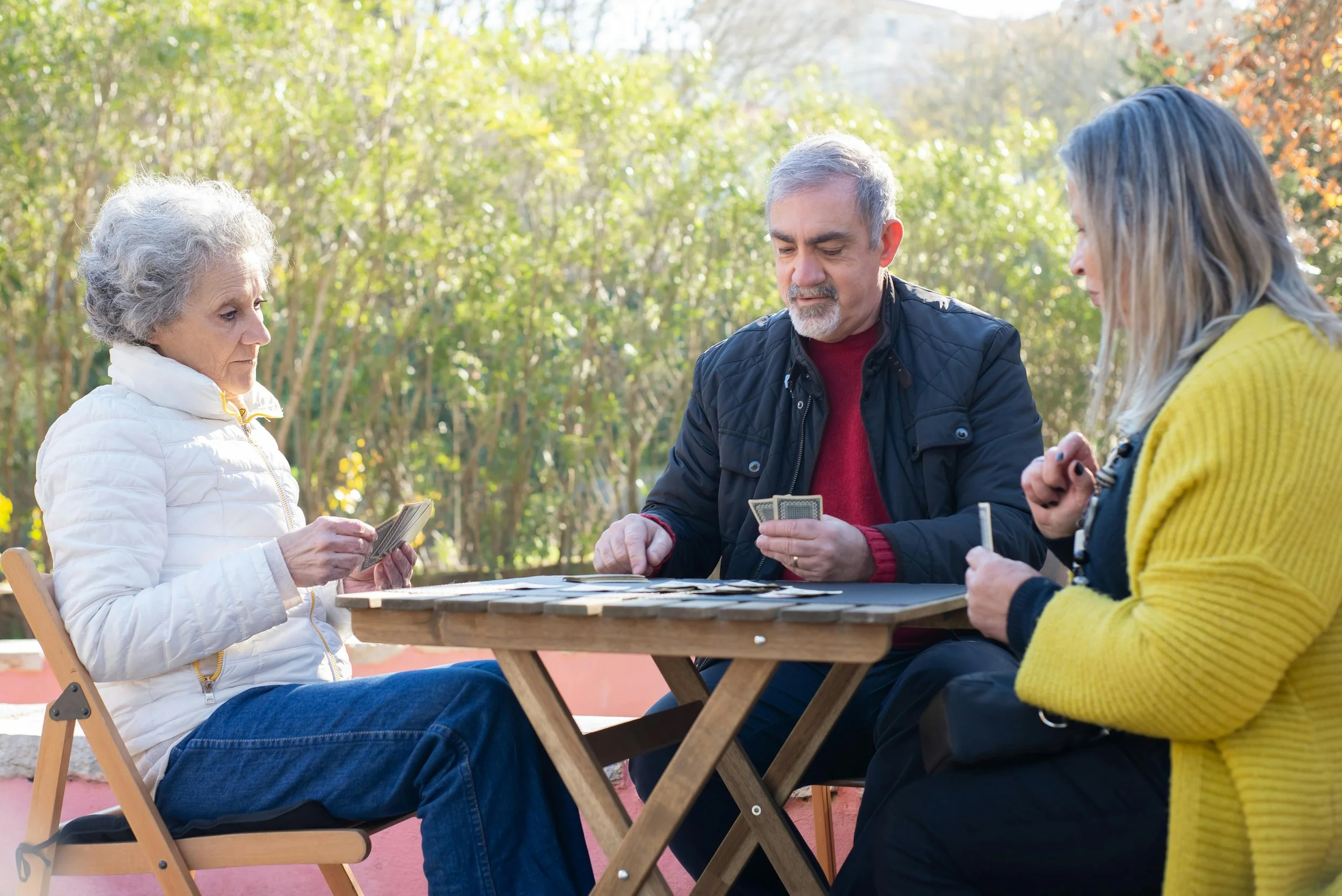 3 mixed age adults playing cards outdoors