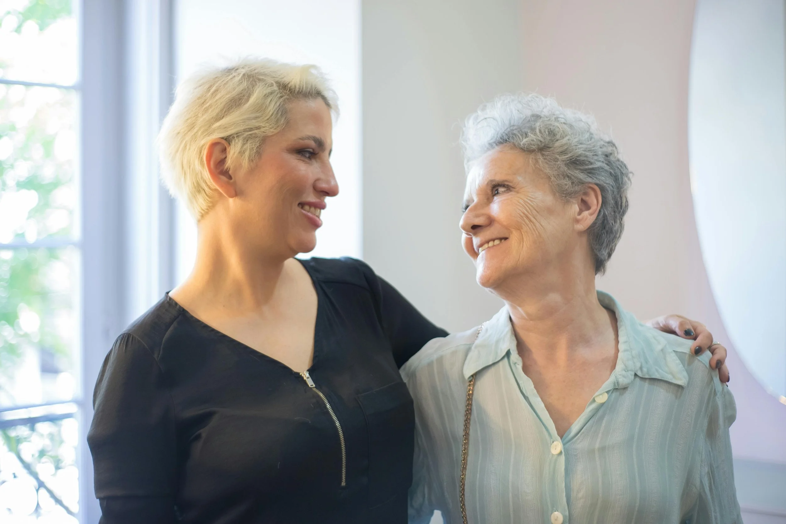 A younger woman and an older woman share a warm smile with an arm around each other, reflecting the trust and connection at the heart of exceptional home care.