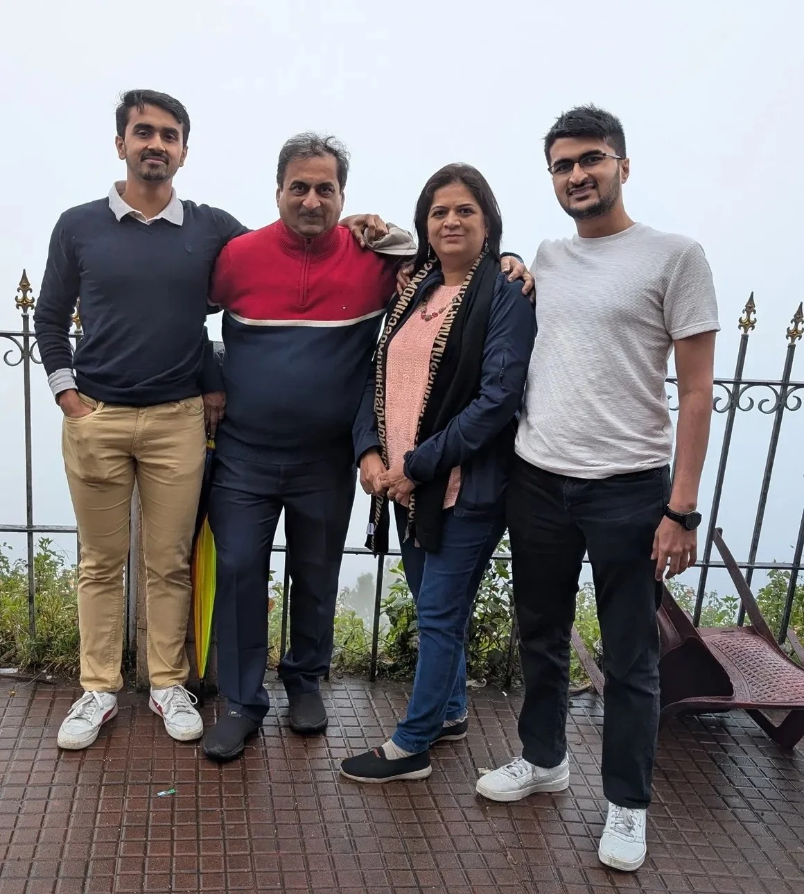 Four people standing outside on a foggy day in front of a metal fence, smiling for the photo.