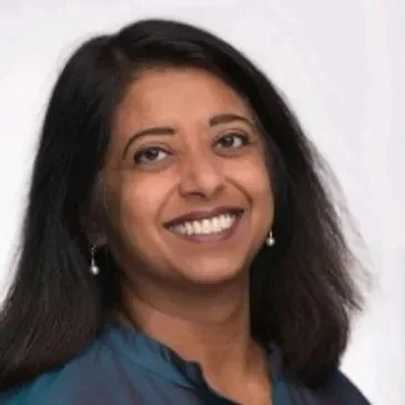 A woman with dark hair smiling against a plain background.