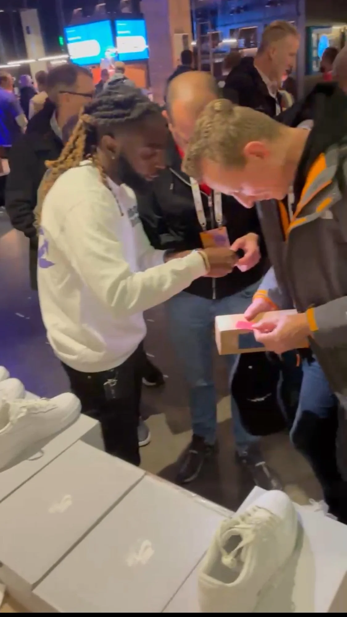 People gathered around a table inside a store, looking at and handling sneakers and shoe boxes, with displayed Nike shoes on the table.