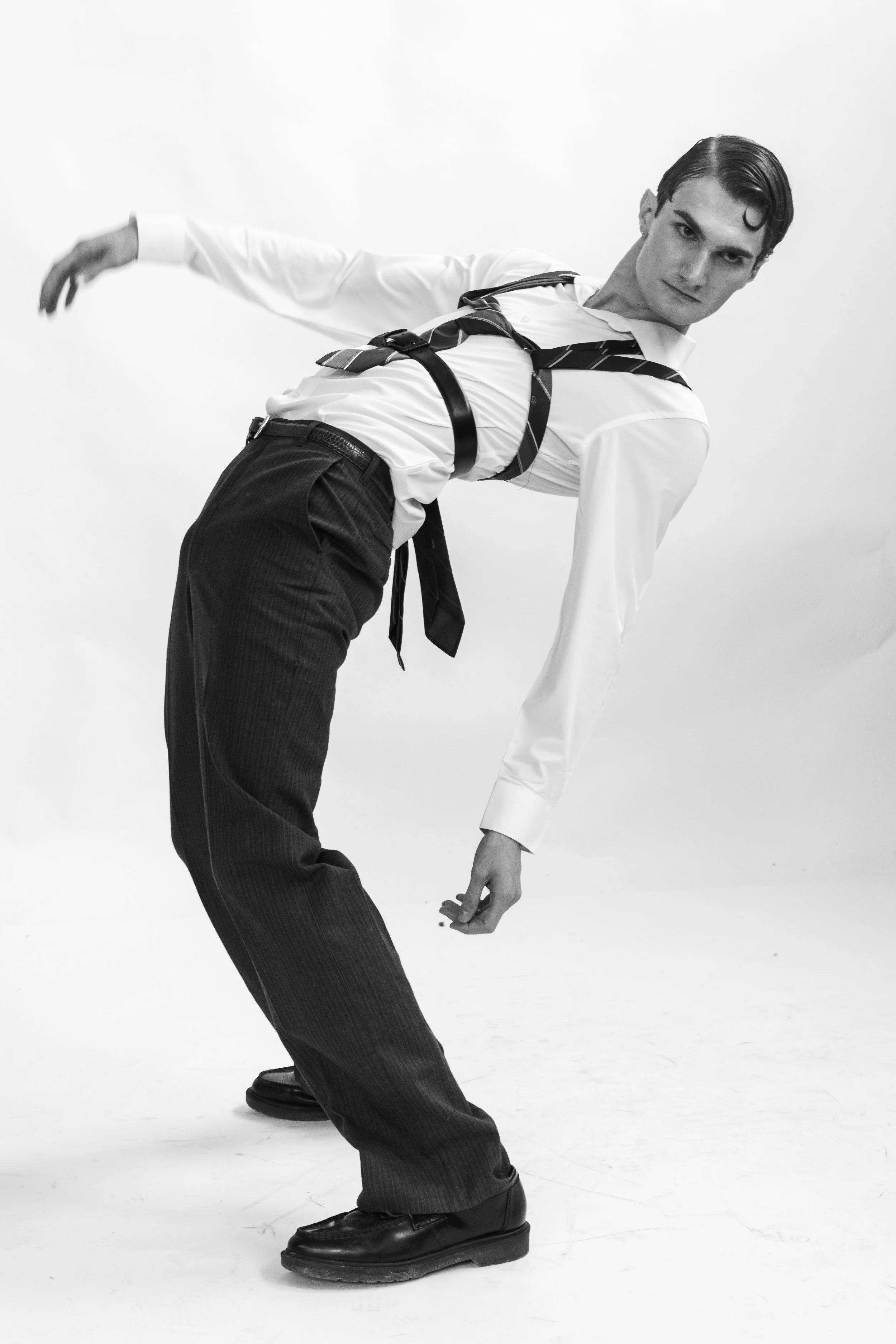 A man wearing formal attire with a patterned tie and suspenders leaning to one side in a black and white photo.
