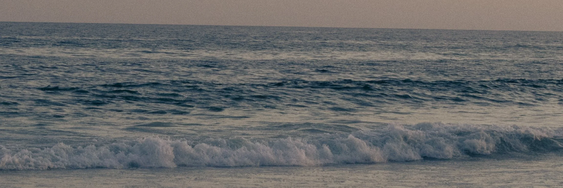 Ocean waves gently crashing on the shore during sunset.