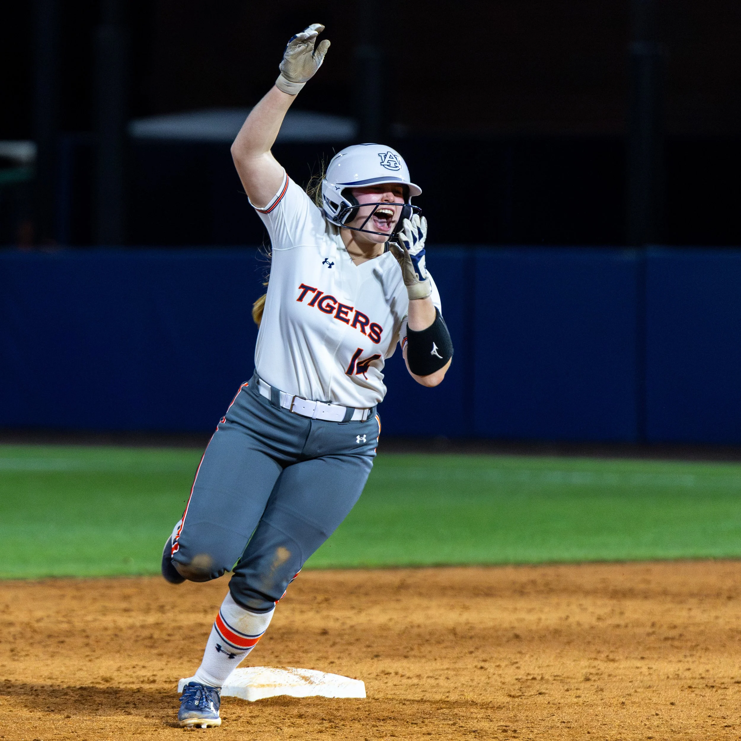 A female softball player in uniform running on the field with a celebrating expression.