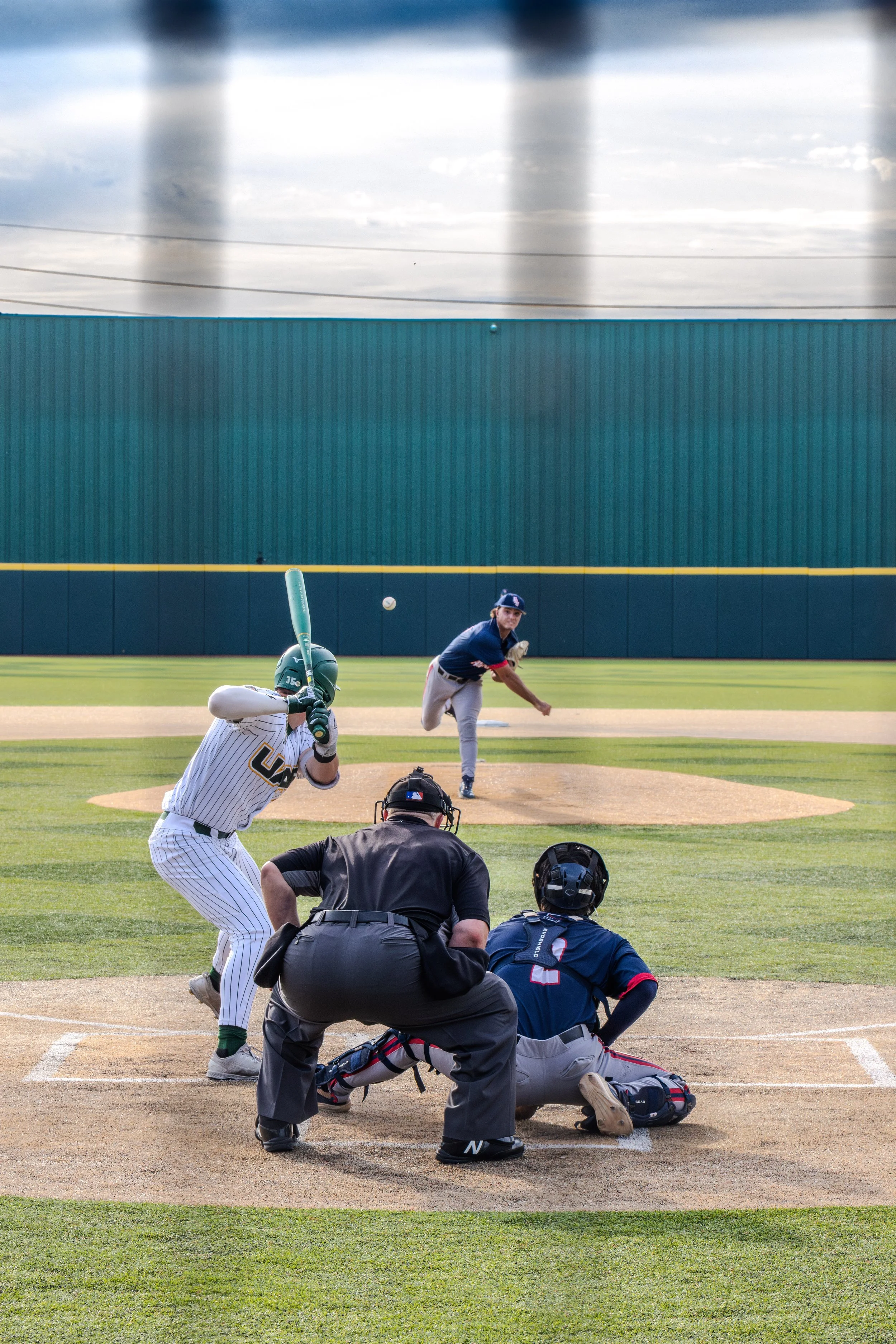 A baseball game in progress with a batter, pitcher, catcher, umpire, and infielder on a baseball field.