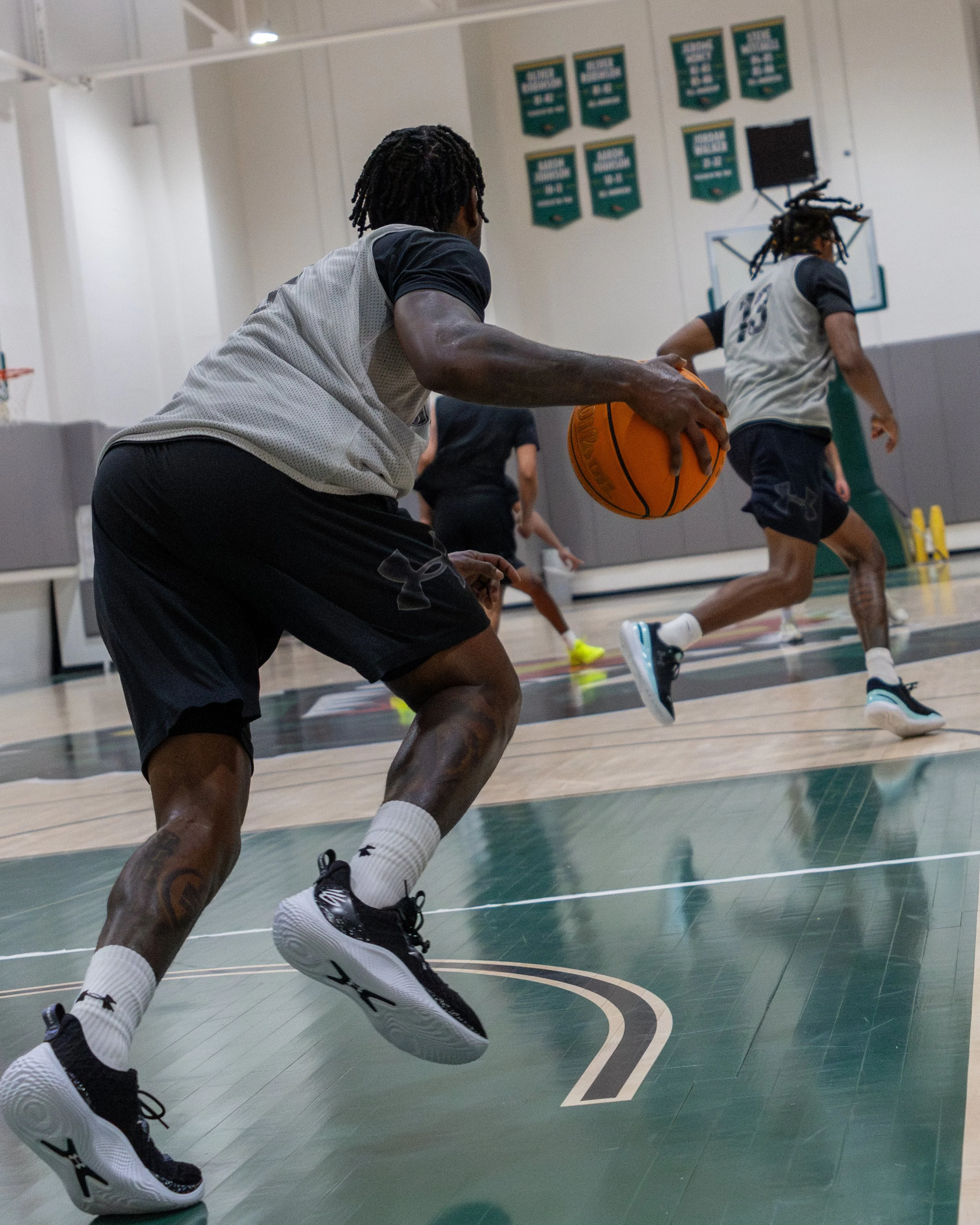A group of basketball players practicing on an indoor court, with one player dribbling the ball while others run behind.