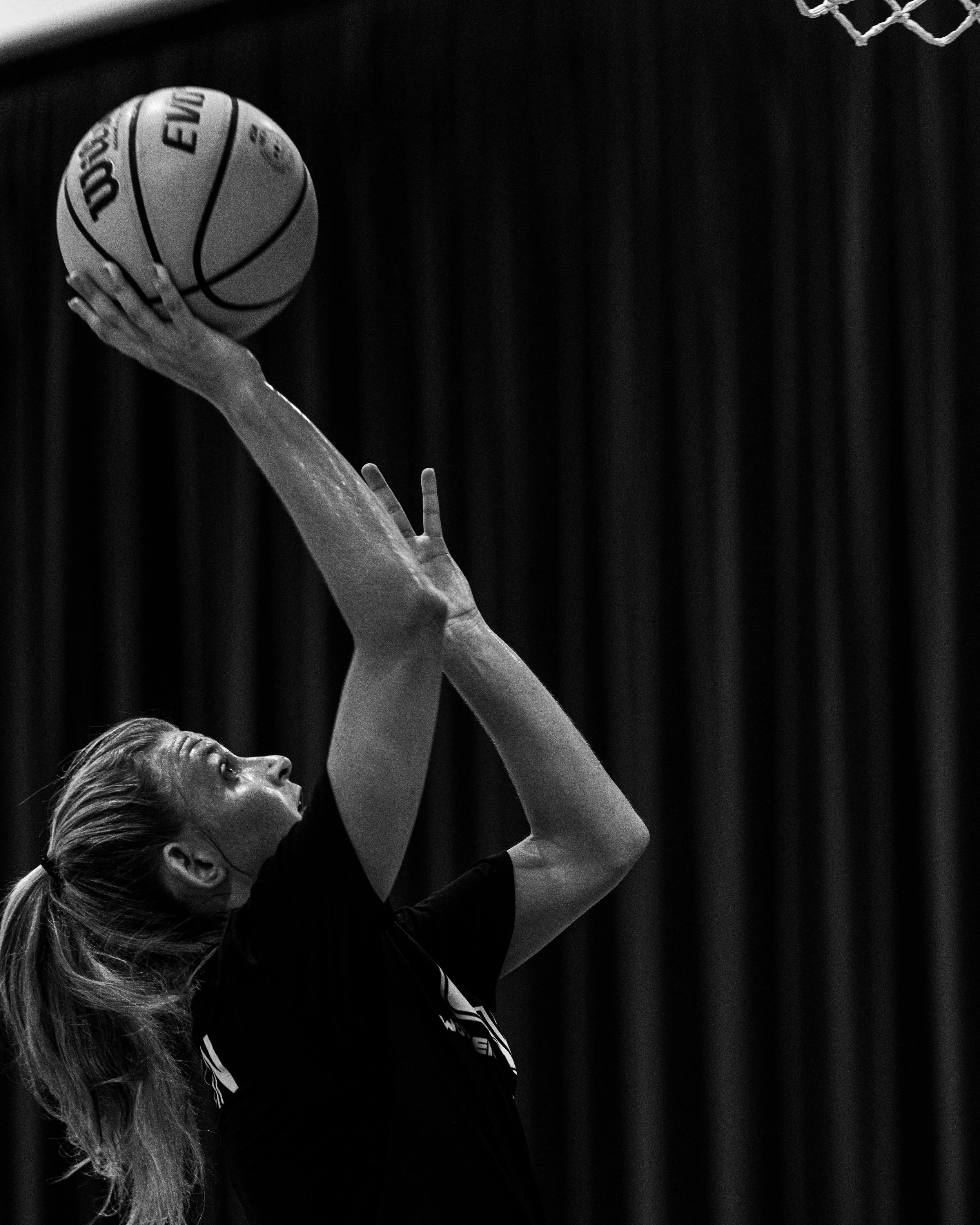 A female athlete with a ponytail preparing to shoot a basketball towards the hoop.