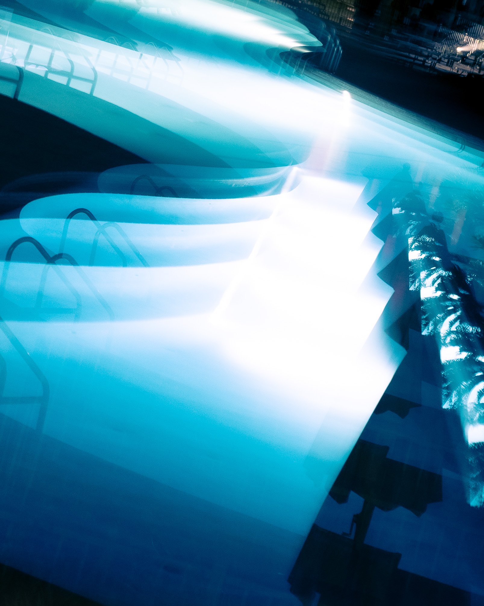 Abstract photo of a modern pool with an ethereal repeating image, with bright white and blue tones, and a palm tree silhouette in the reflection.