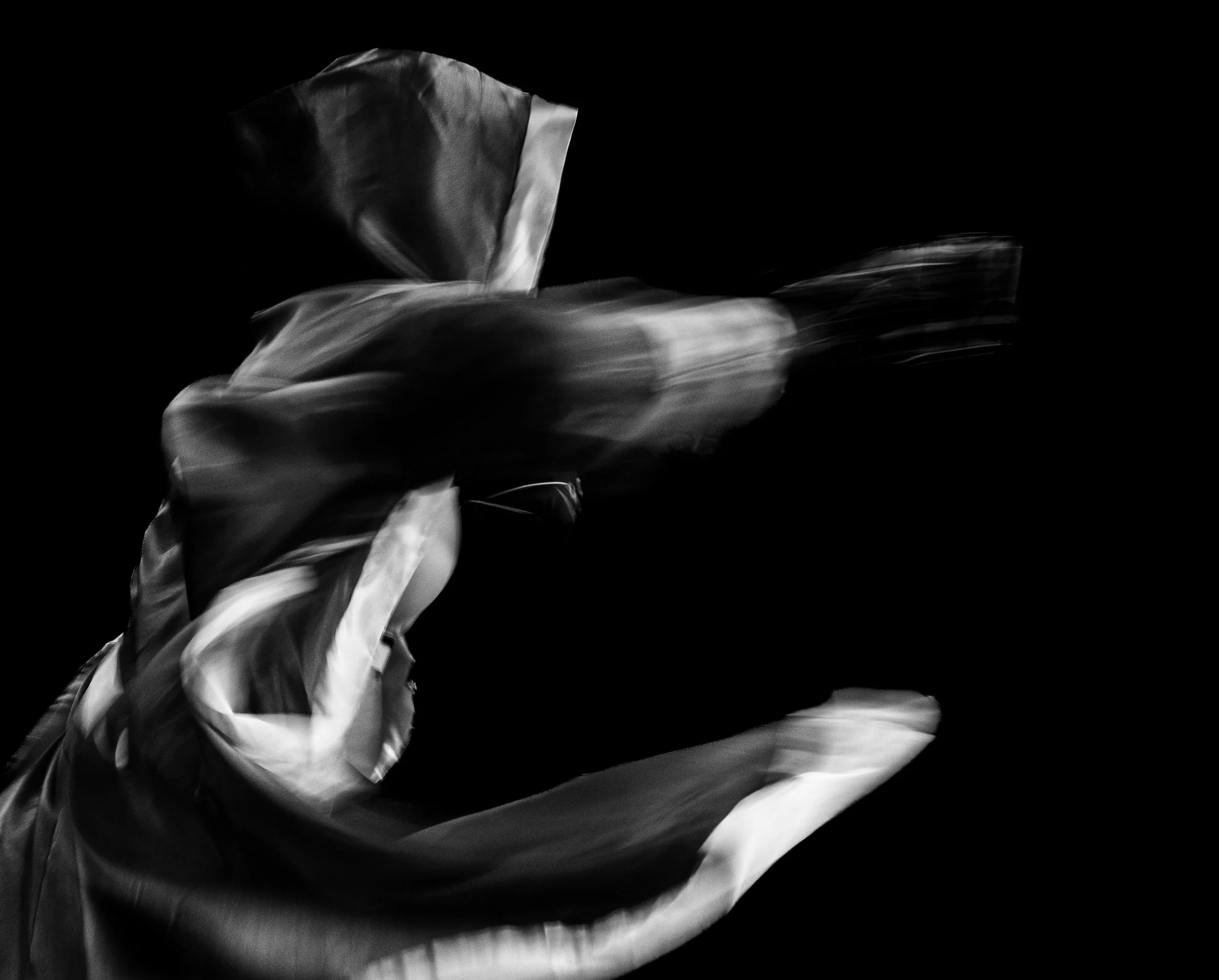 Black and white photo of a person throwing a jab with flowing fabric against a dark background.