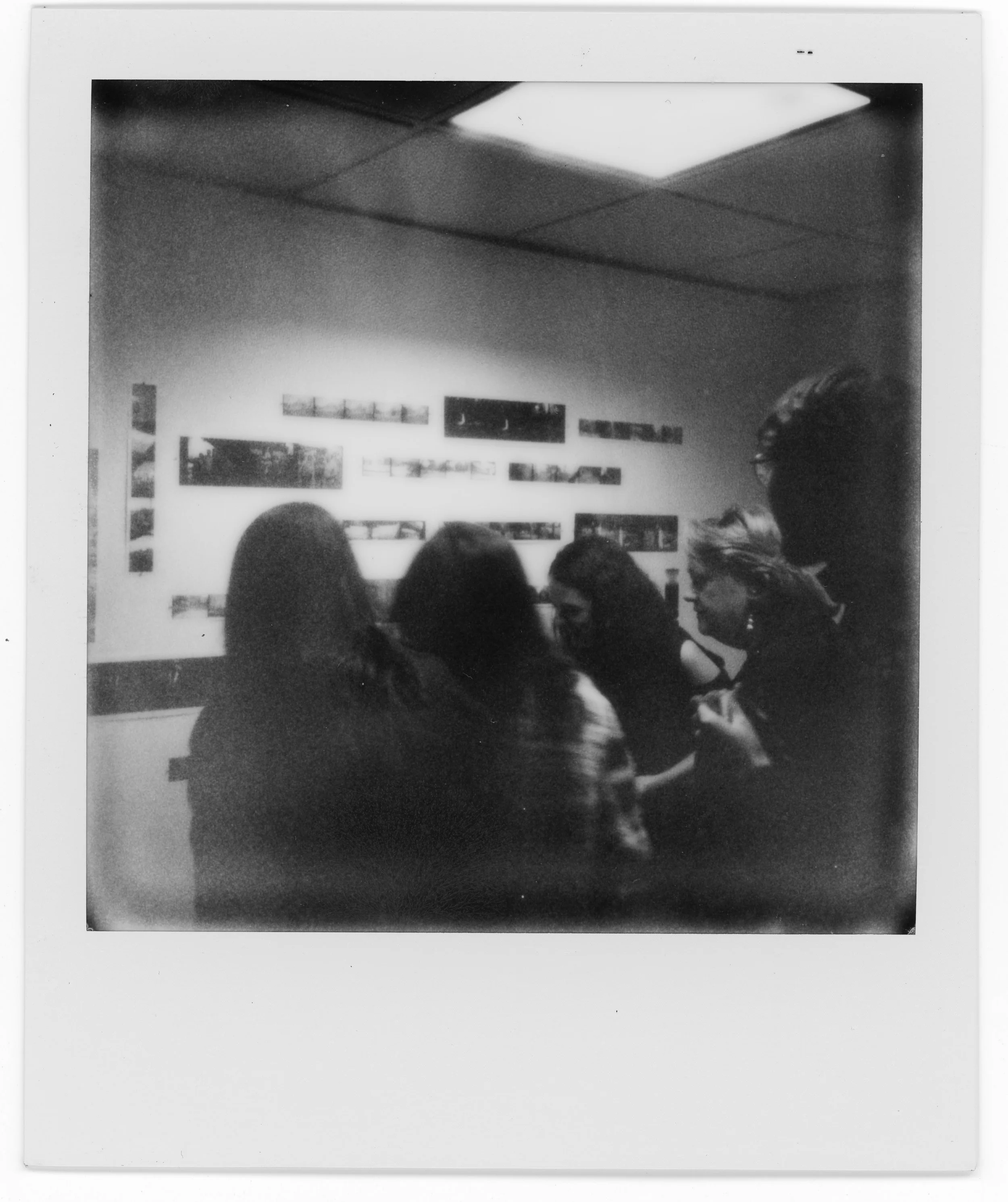A group of four young women and one young man standing and talking in an art gallery with photographs on the wall in front of them.