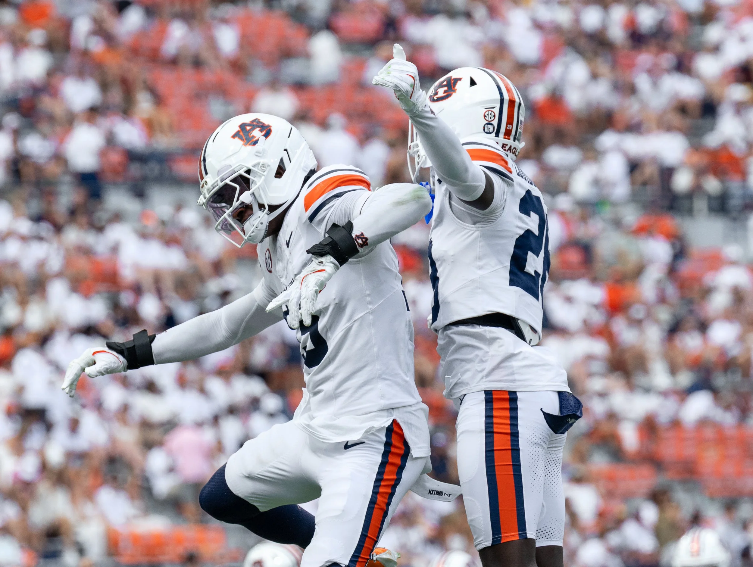 Two Auburn football players celebrating on the field during a game with a crowd of spectators in the background.