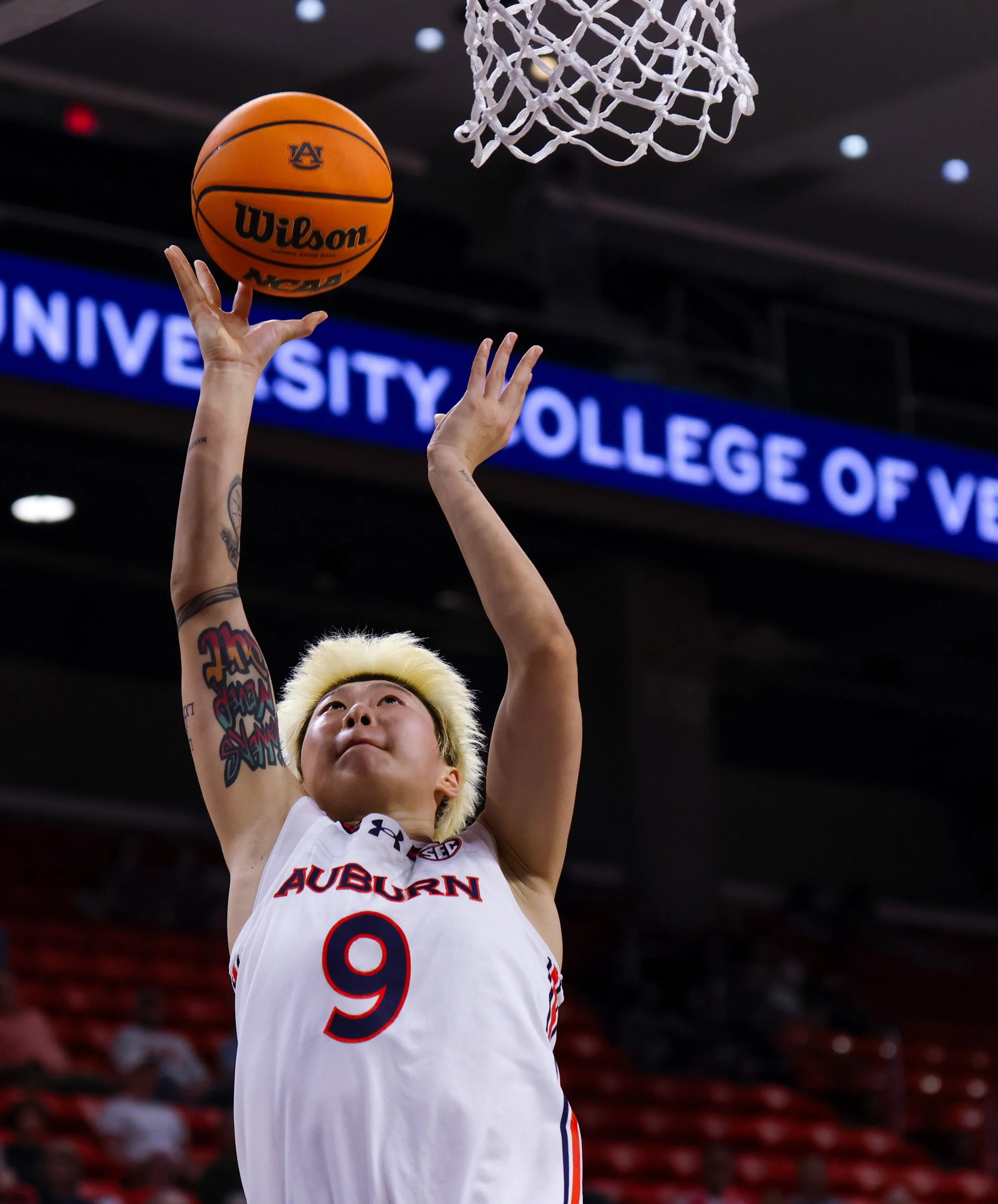 A female basketball player from Auburn University wearing jersey number 9 is making a shot towards the hoop in an indoor basketball court.