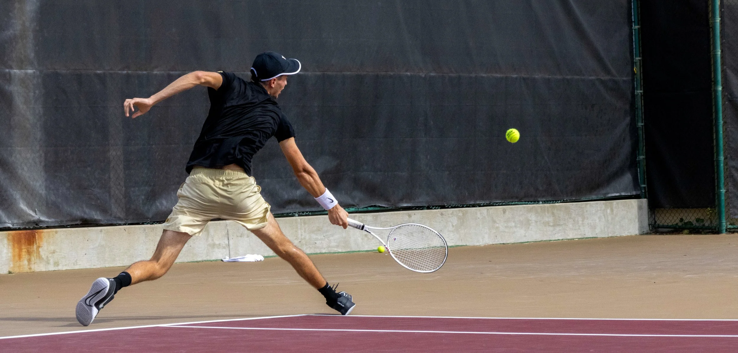 A man playing tennis on an outdoor court, preparing to hit a yellow tennis ball with a racket.