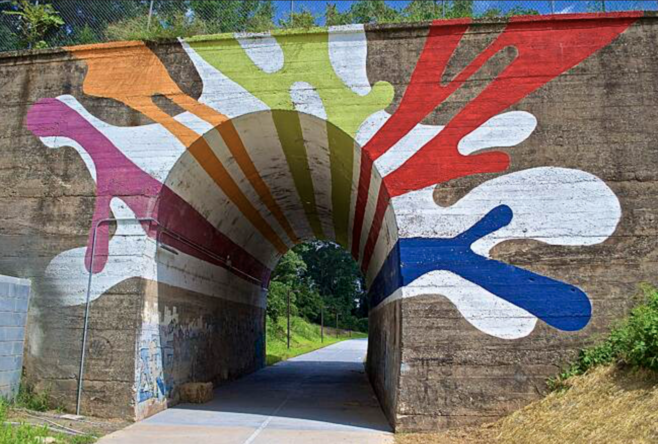 Colorful abstract mural painted on a tunnel wall with splashes of pink, orange, green, red, and blue extending from the entrance, resembling paint splatters.