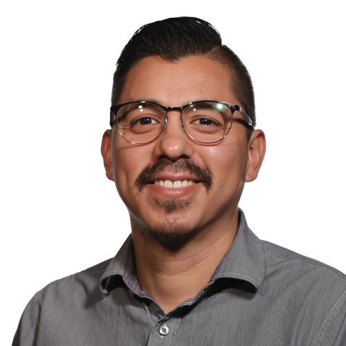 A smiling man wearing glasses and a gray collared shirt against a white background.