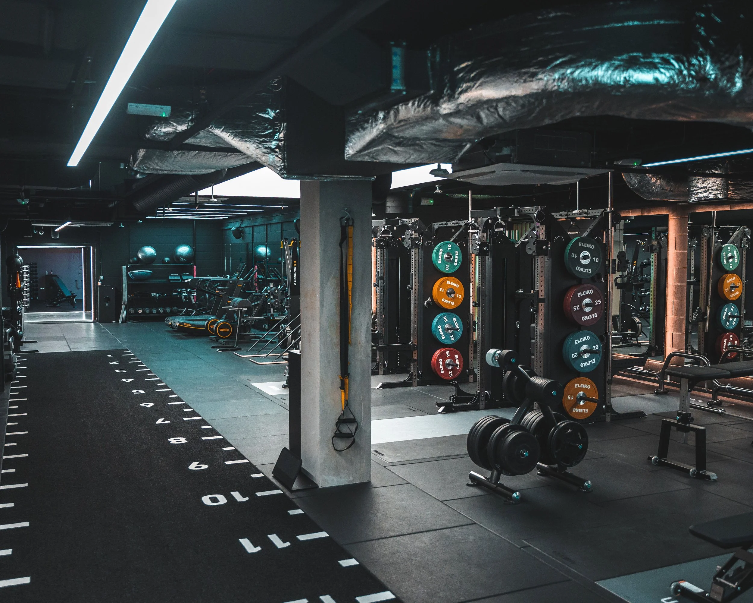 Interior of a modern gym with weightlifting equipment, exercise machines, and a designated running track area.