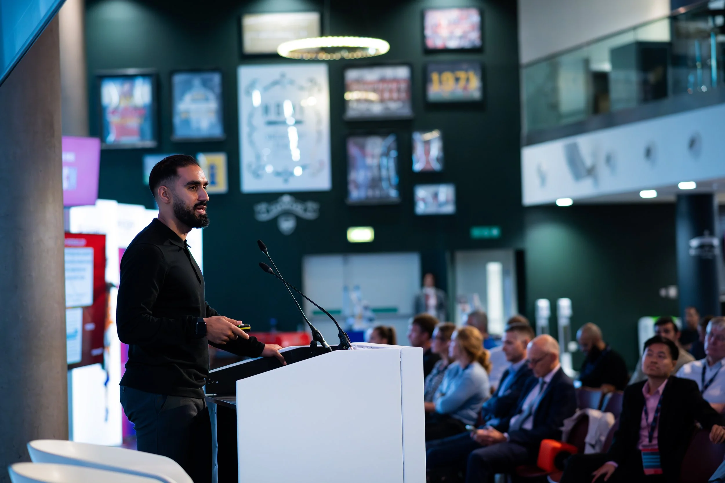 A man giving a presentation at a conference with an audience seated in front of him.
