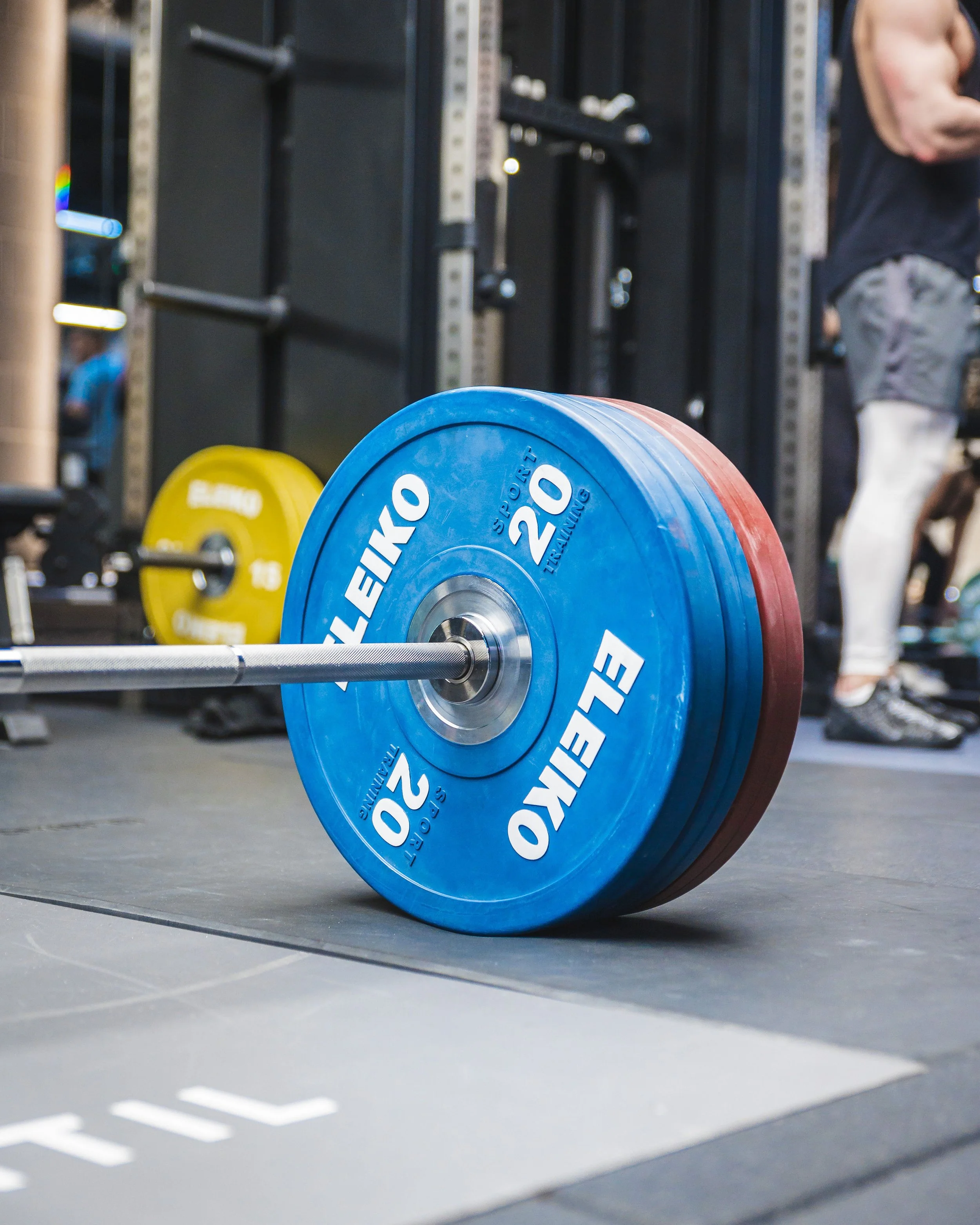 Close-up of a loaded barbell with blue and yellow weight plates in a gym setting.