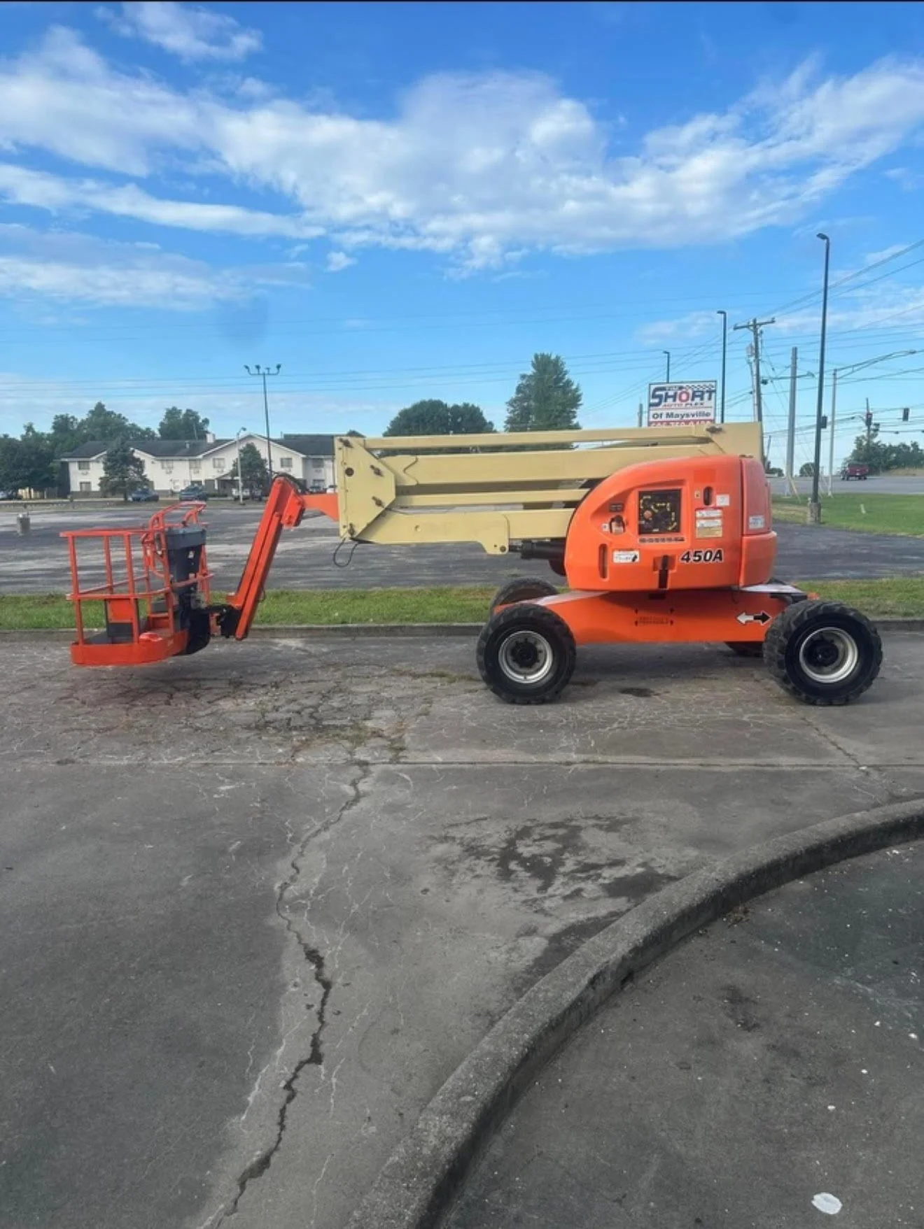 An orange cherry picker parked outdoors on a paved surface with a blue sky backdrop.