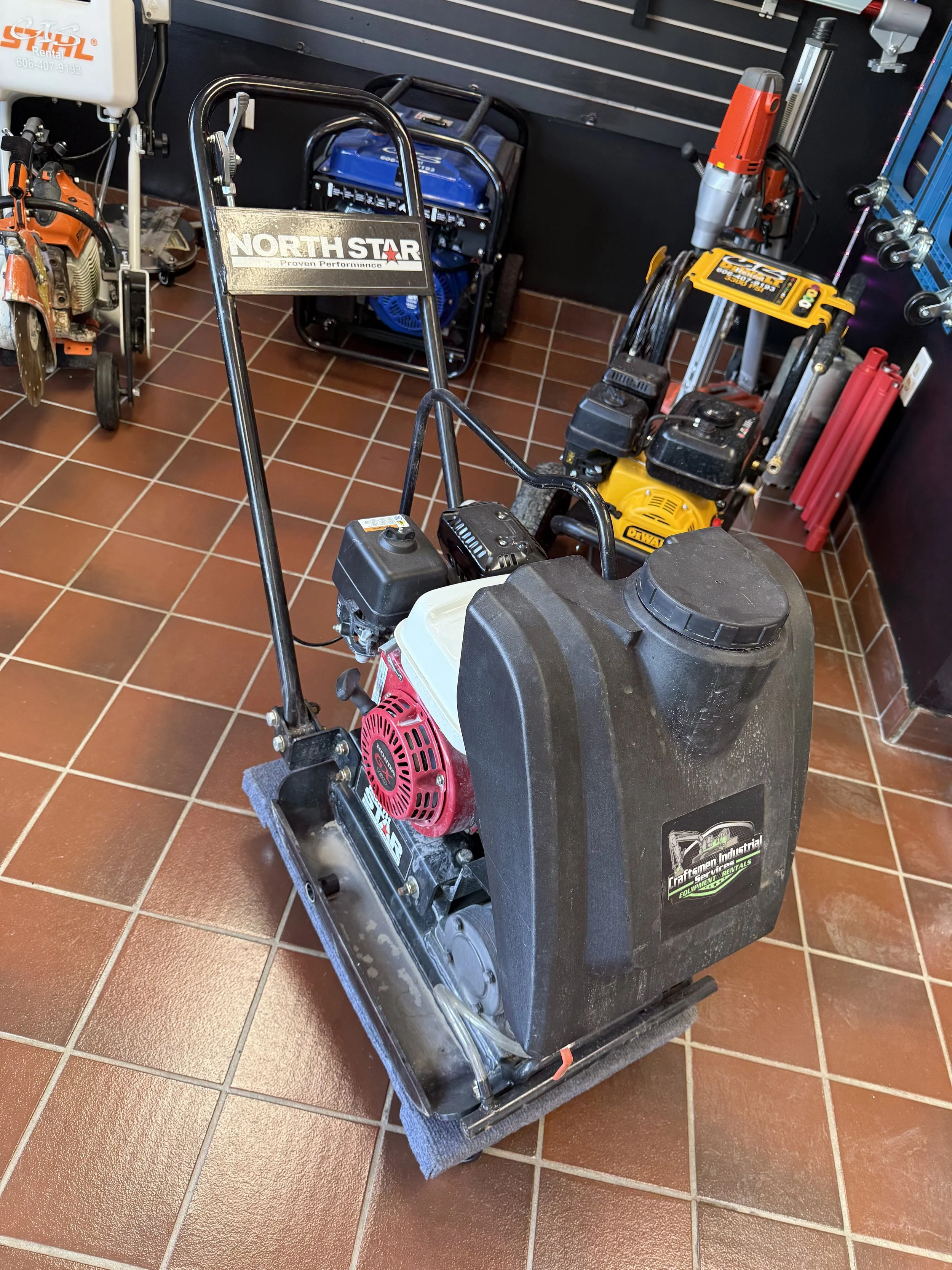 Plate compactor with "NorthStar" brand label in a store display, surrounded by other equipment, on a tiled floor.