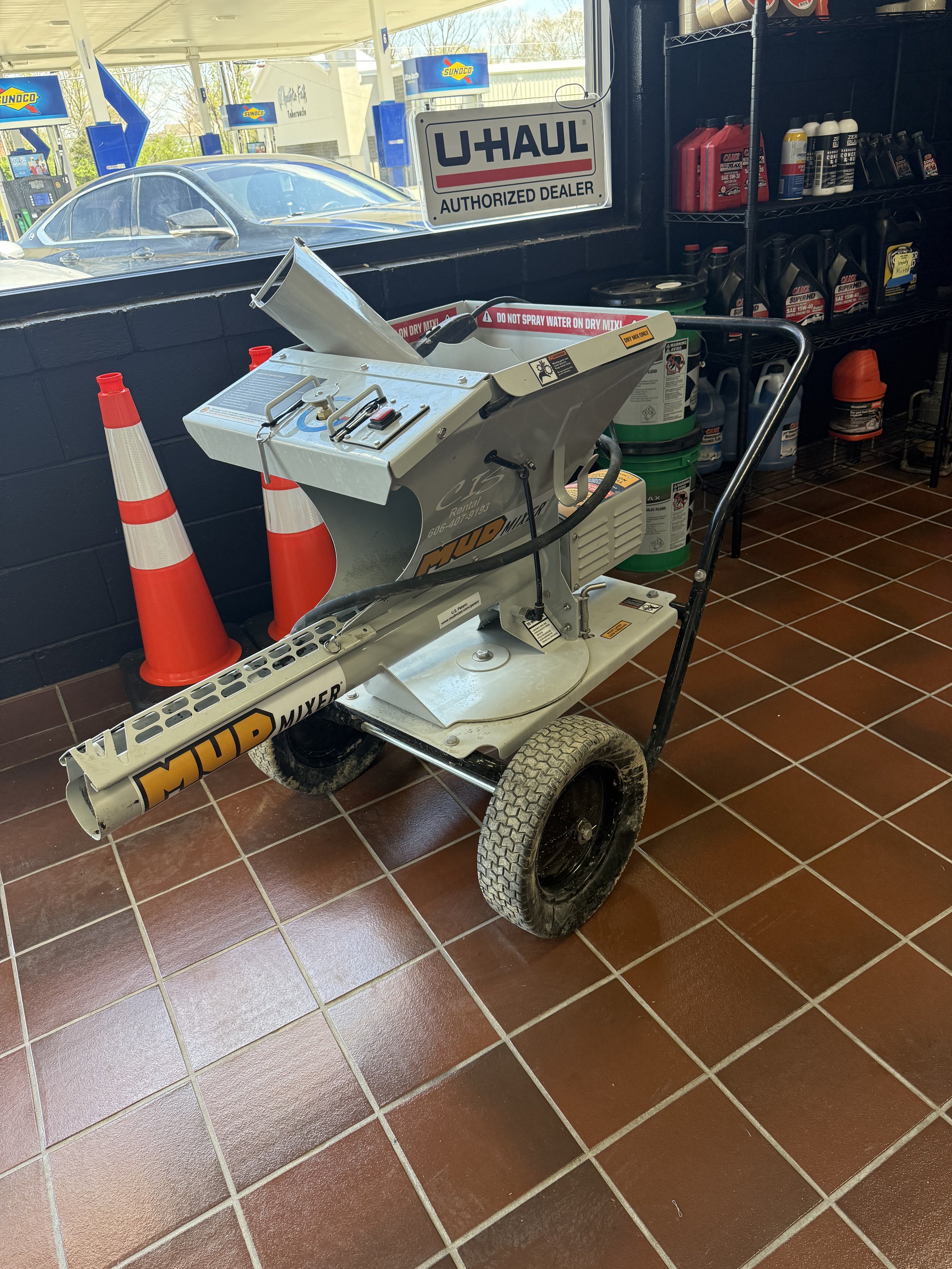 Mud mixer machine on wheels, located inside a store with U-Haul sign and assorted automotive products on shelves in the background.