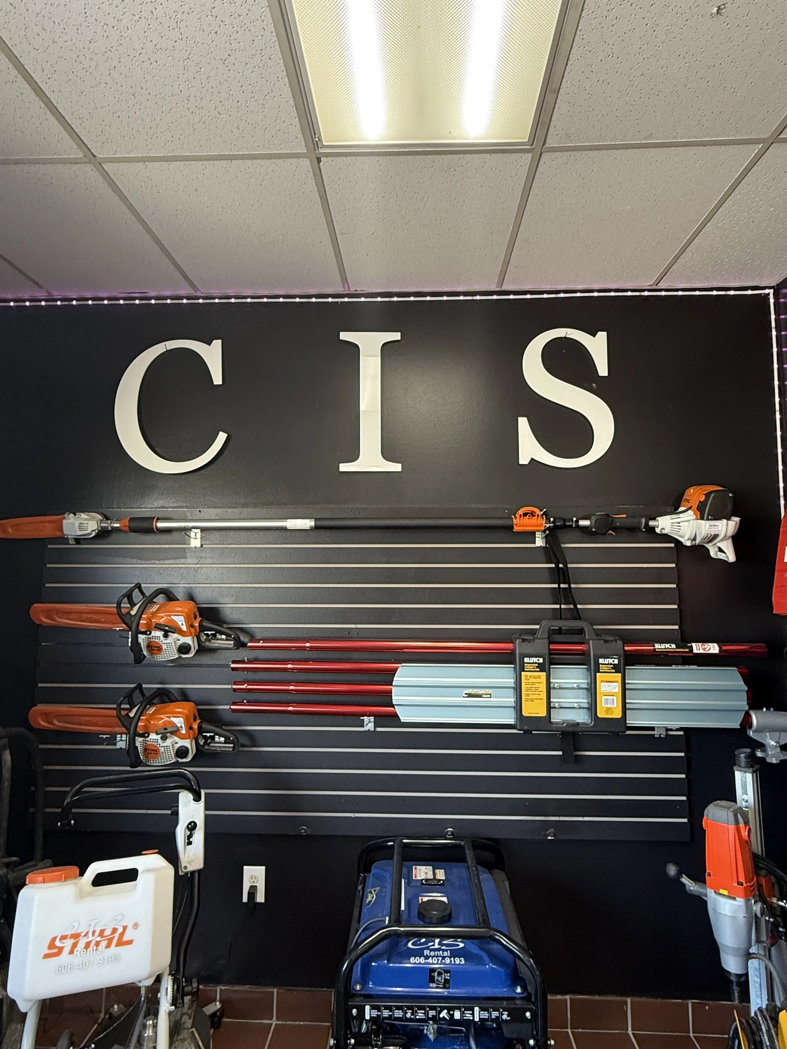 Wall display of various tools and equipment like chainsaws and poles against a black background with 'CIS' written on the wall.