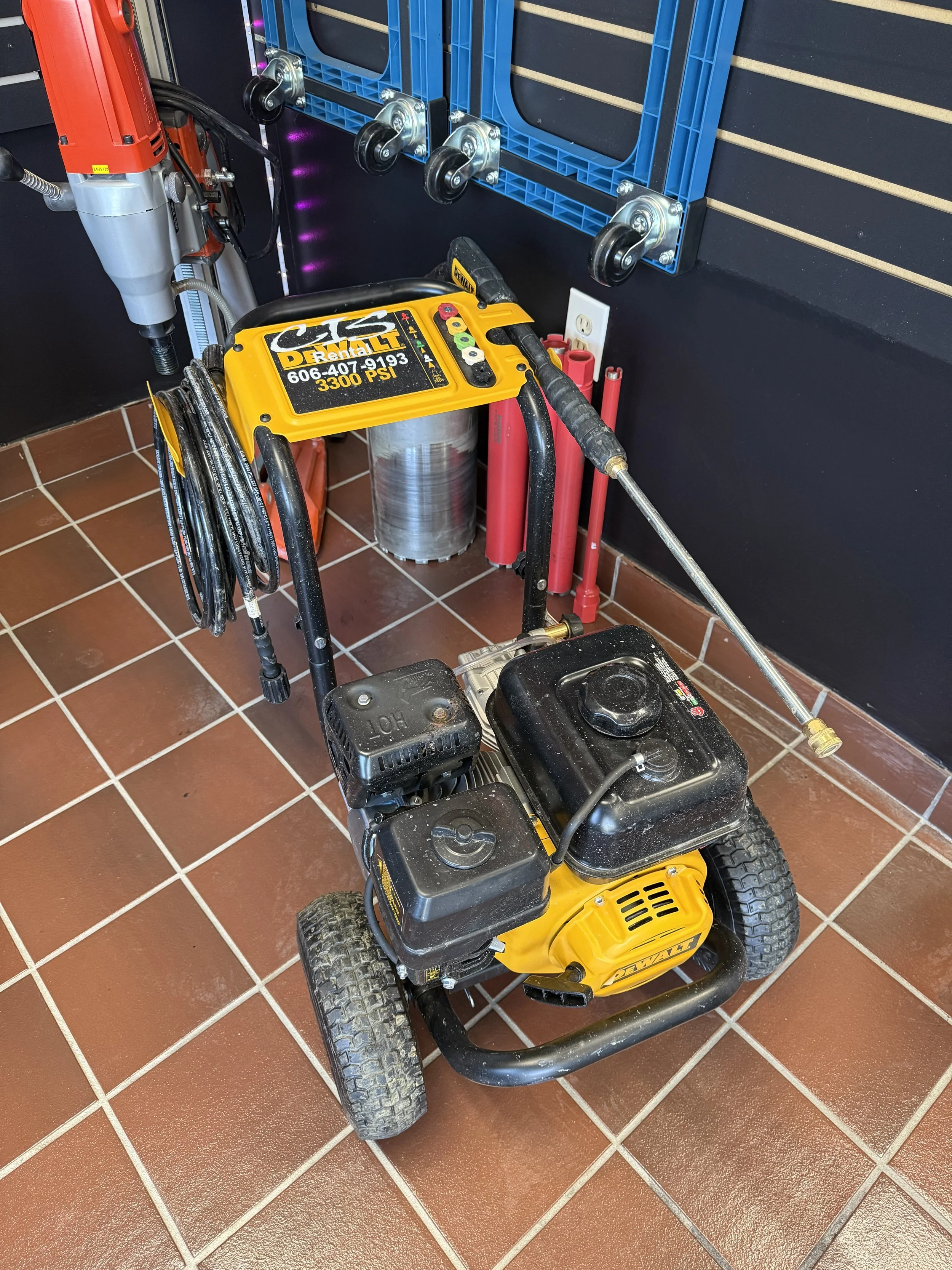 Pressure washer with yellow body and hose on tiled floor in a shop setting.