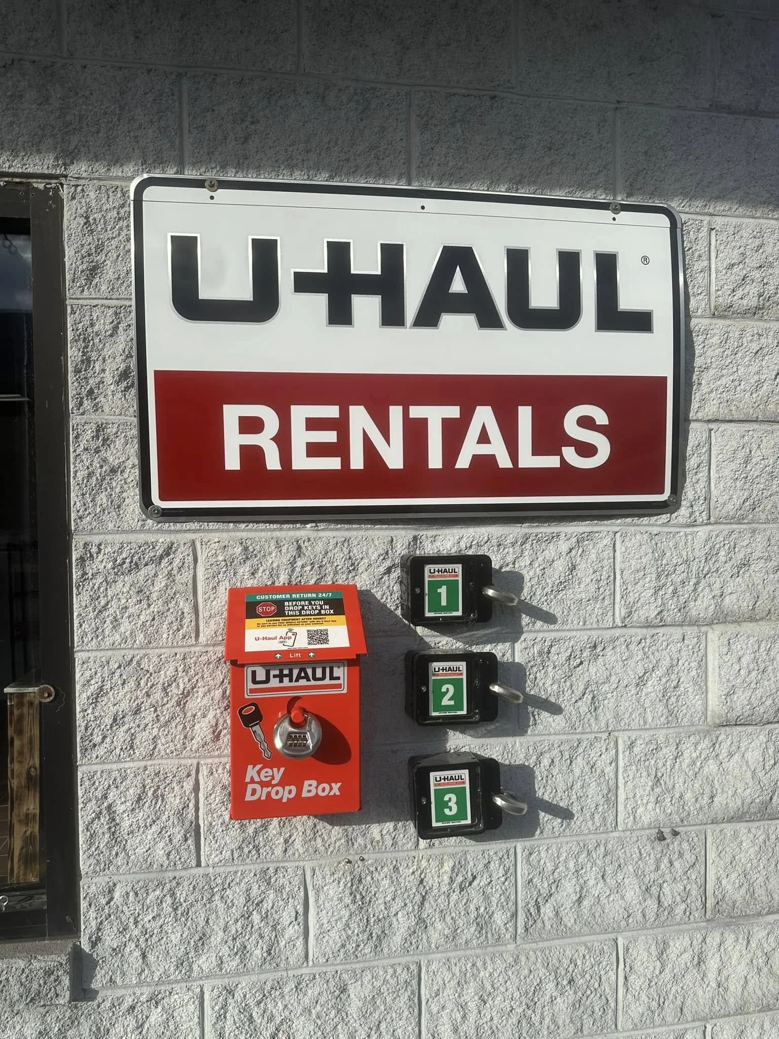 Sign for U-Haul rentals on a brick wall with a key drop box and numbered lockboxes.