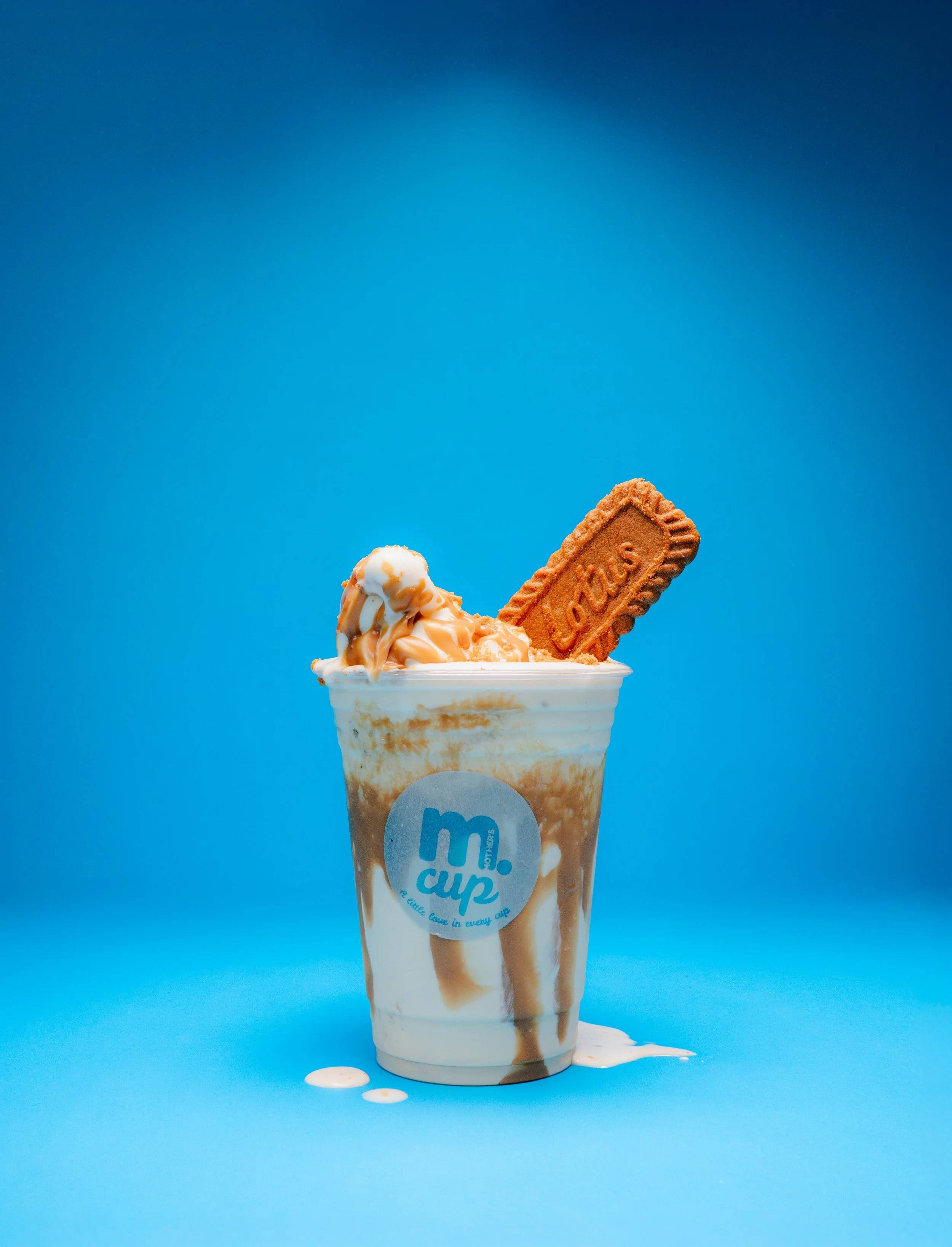 Ice cream in a cup with caramel sauce, a biscuit, and a blue background.