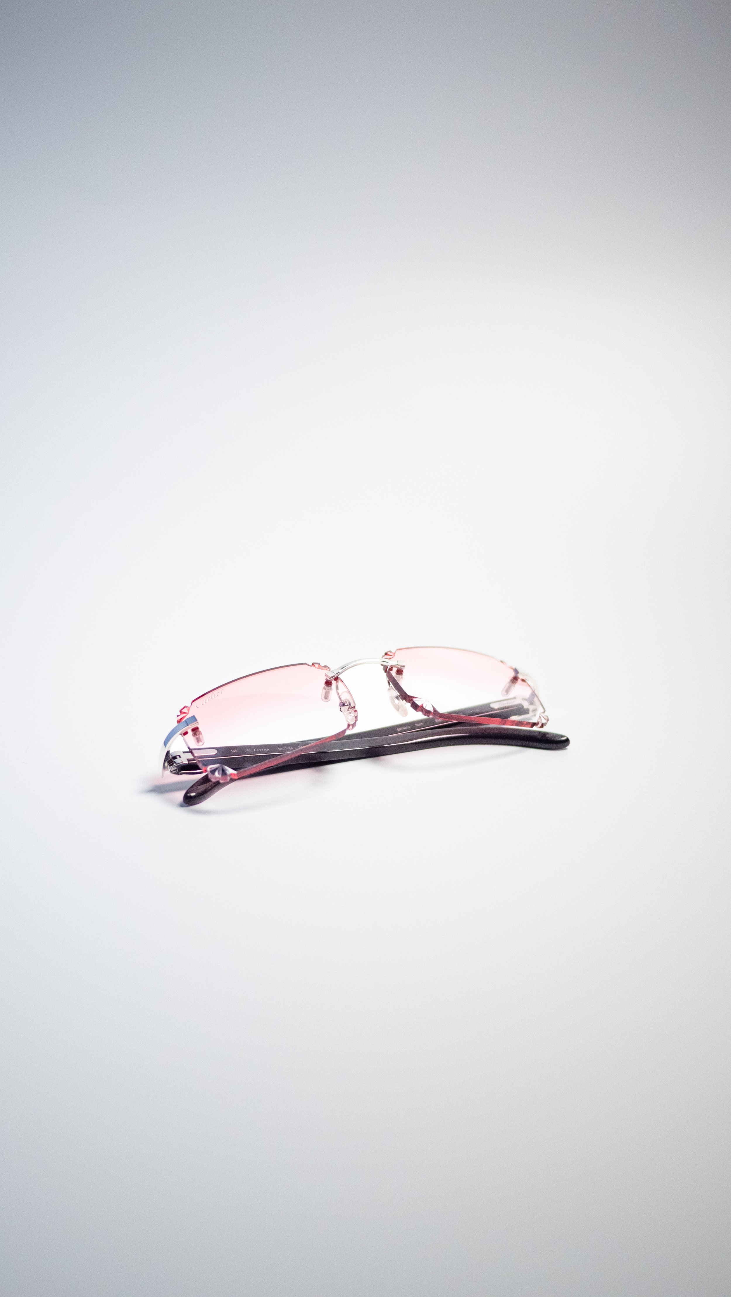 A pair of eyeglasses with pink-tinted lenses and black temples on a plain white background.