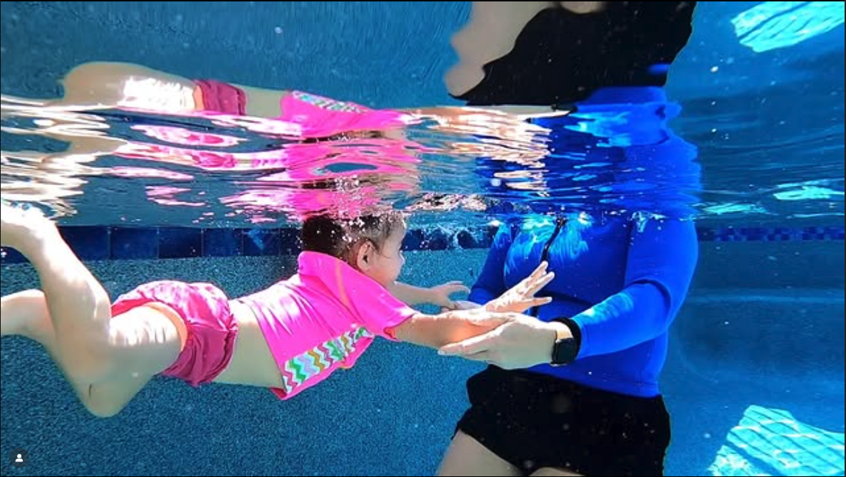 Child swimming underwater with an adult in a pool