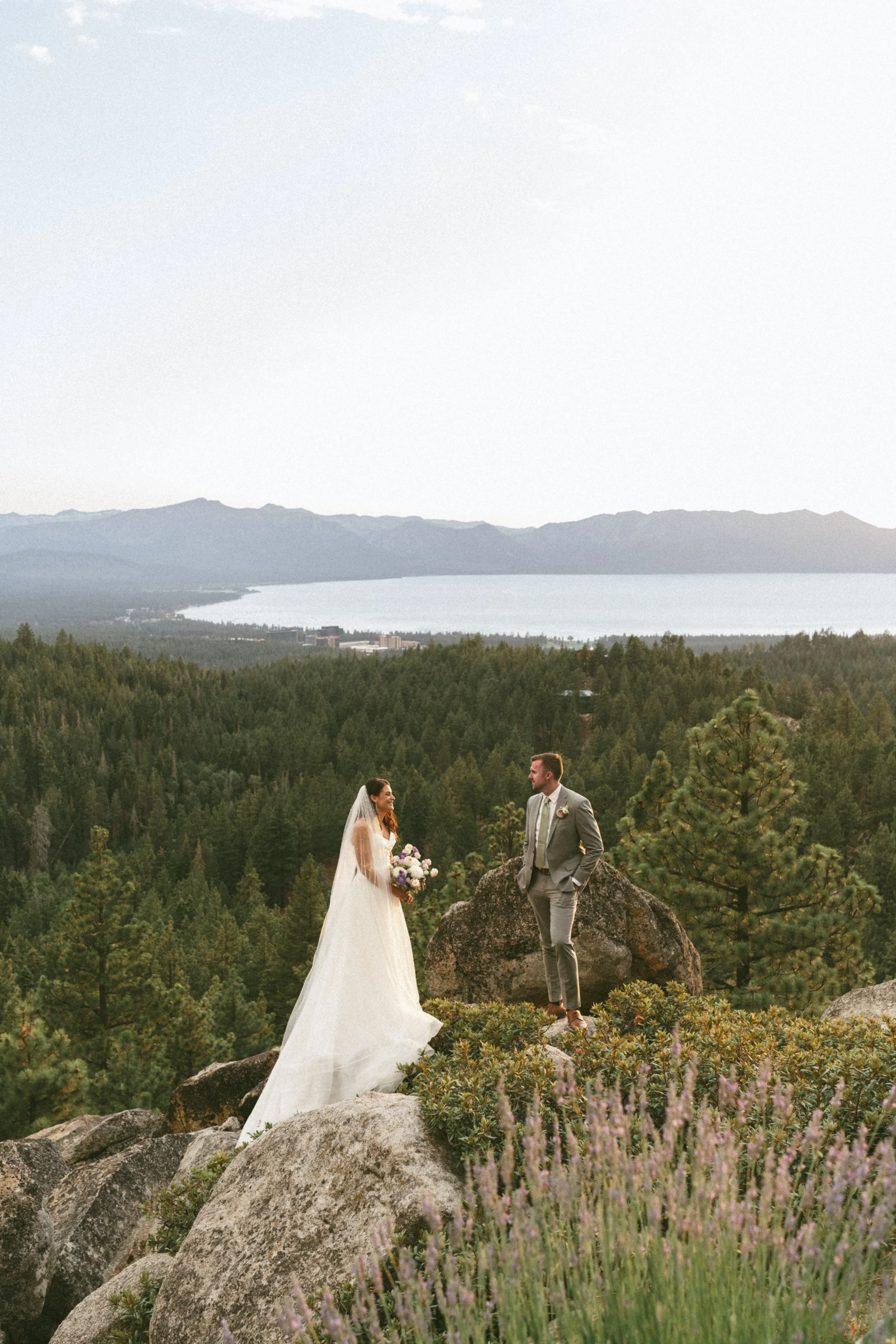 BRIDE AND GROOM STANDING ON MOUNTAIN IN FRONT OF LAKE TAHOE