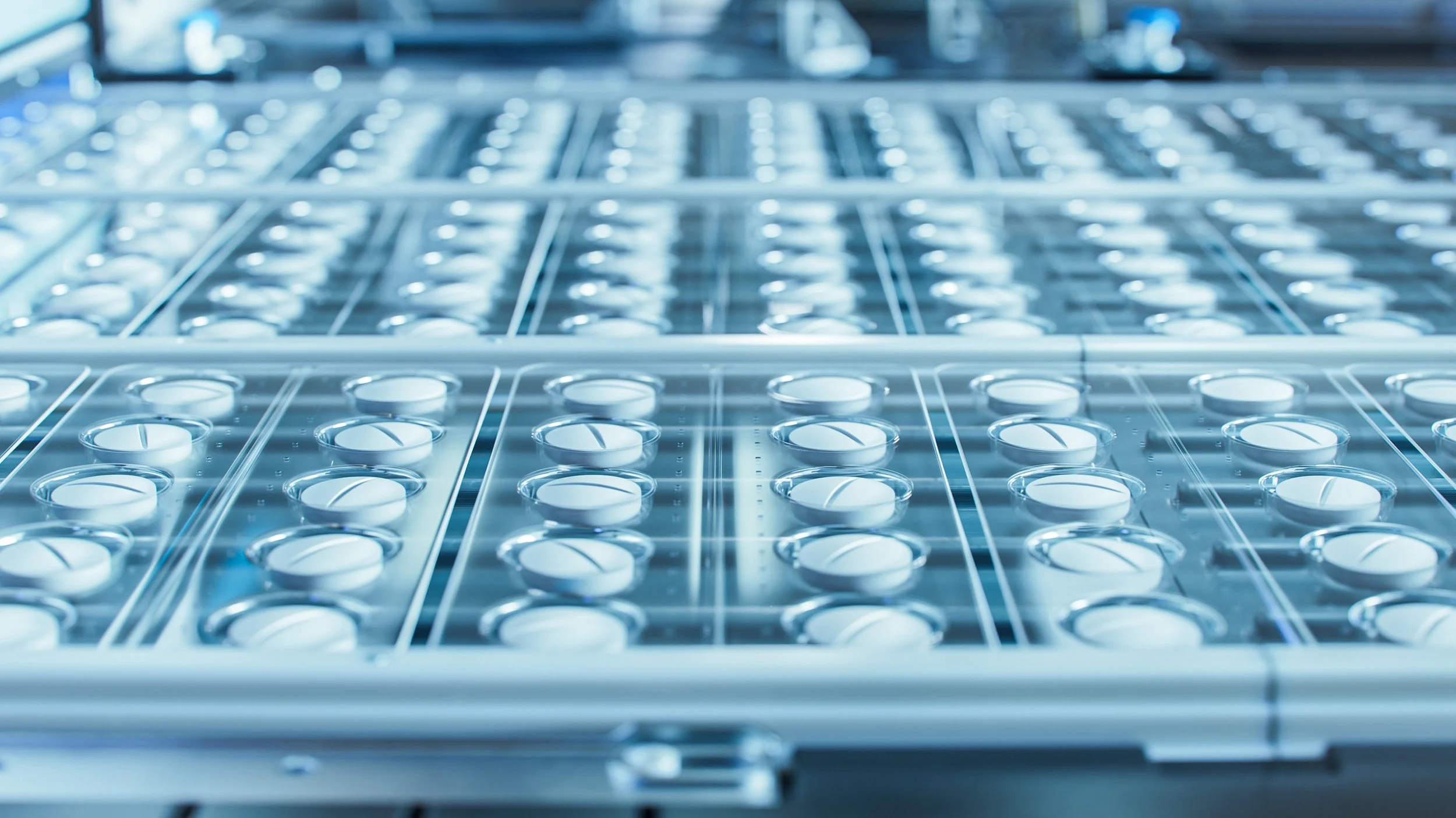 Multiple trays filled with white pills in a pharmaceutical manufacturing setting.