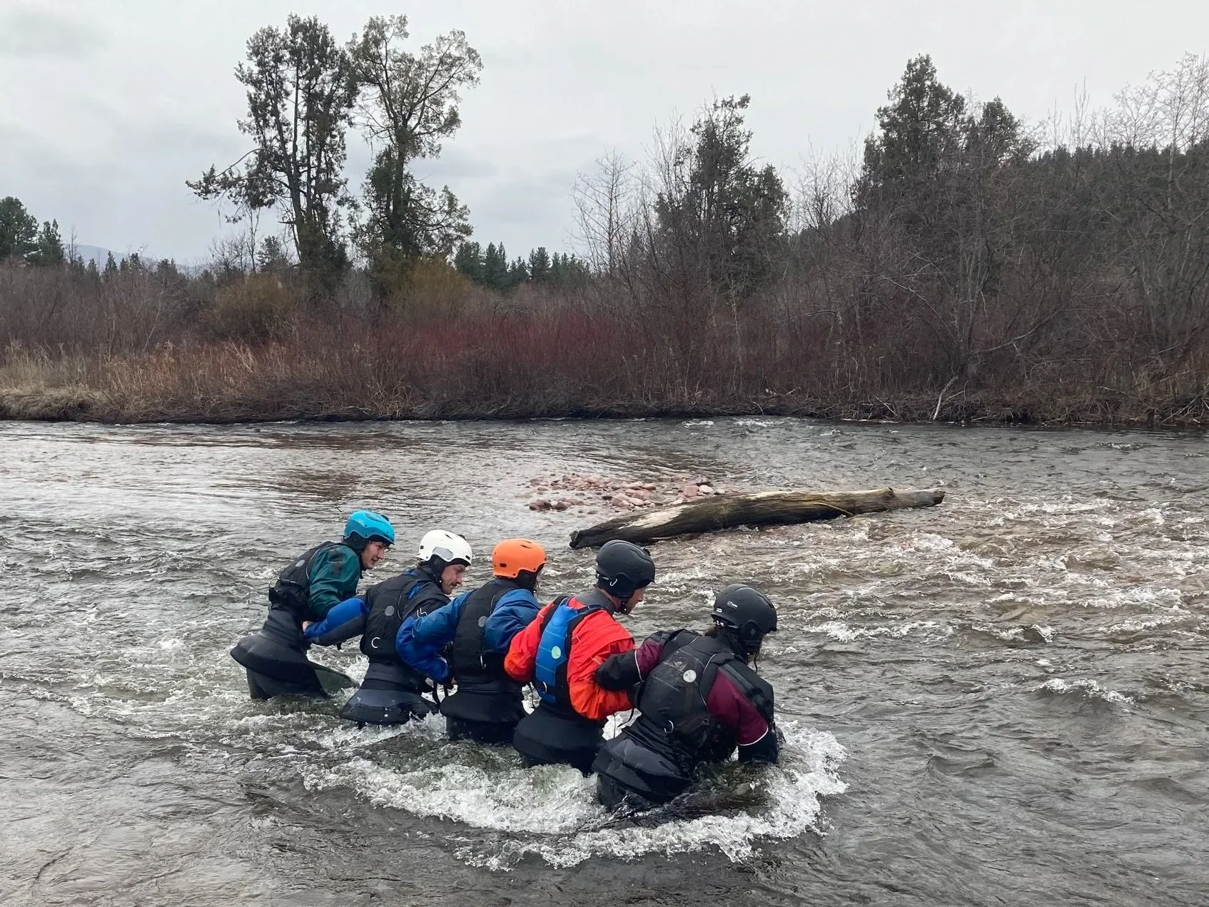 A group of men and women in kayaking gear in a swift water rescue course in Western Montana performing a shallow water crossing drill