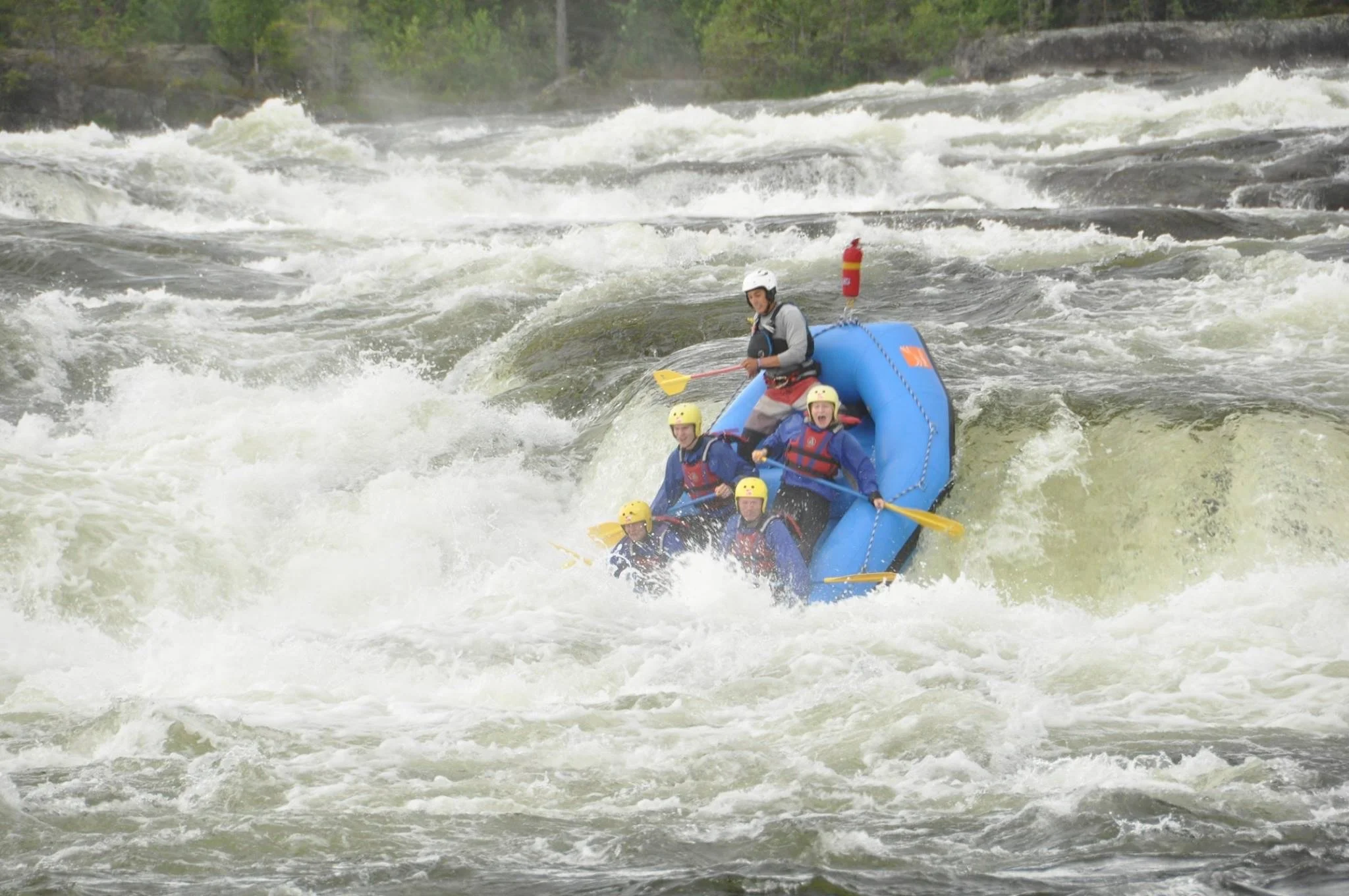 People white-water rafting on a turbulent river surrounded by dense green trees and rocky banks.
