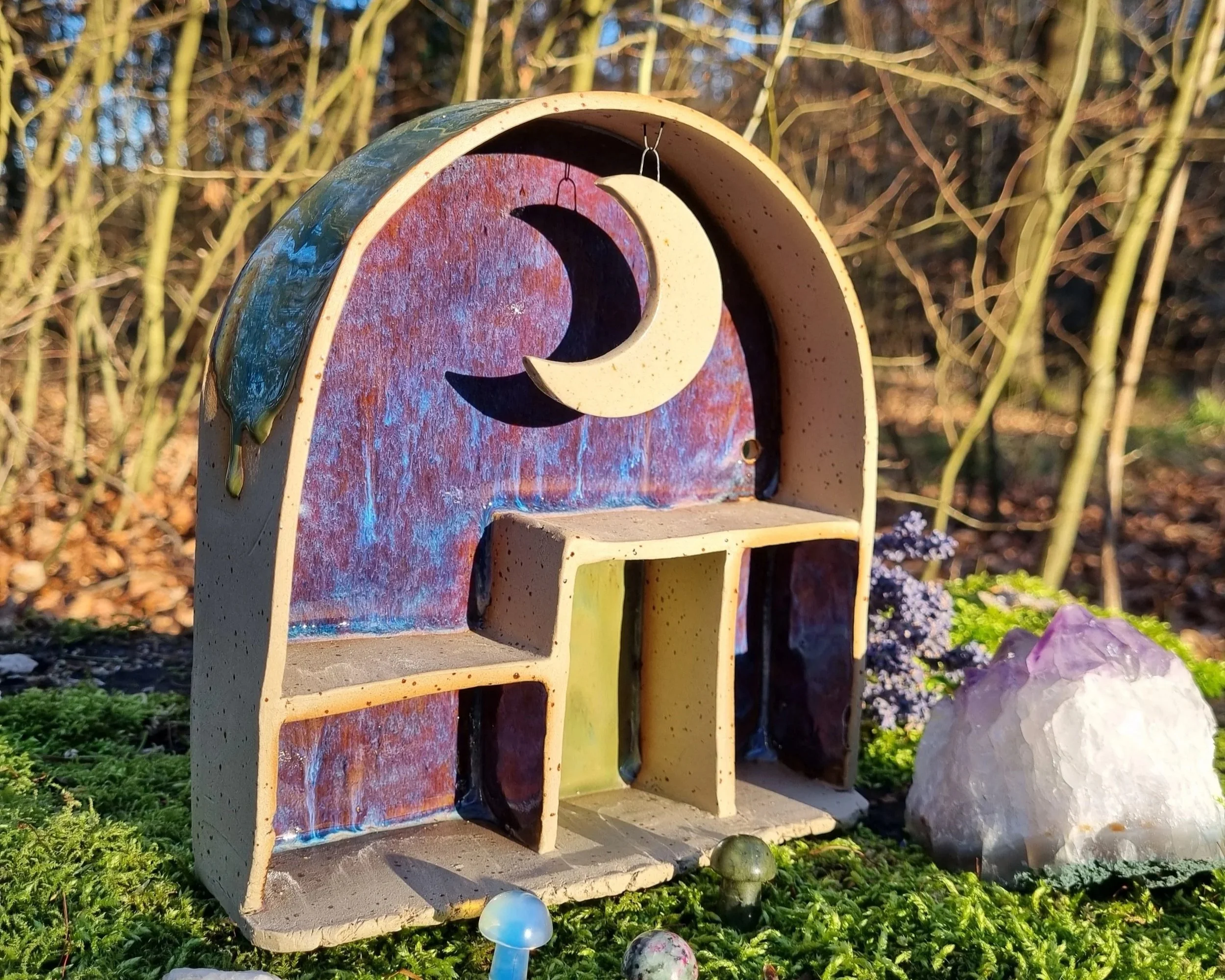 A decorative ceramic piece with a crescent moon hanging inside a rainbow arch.