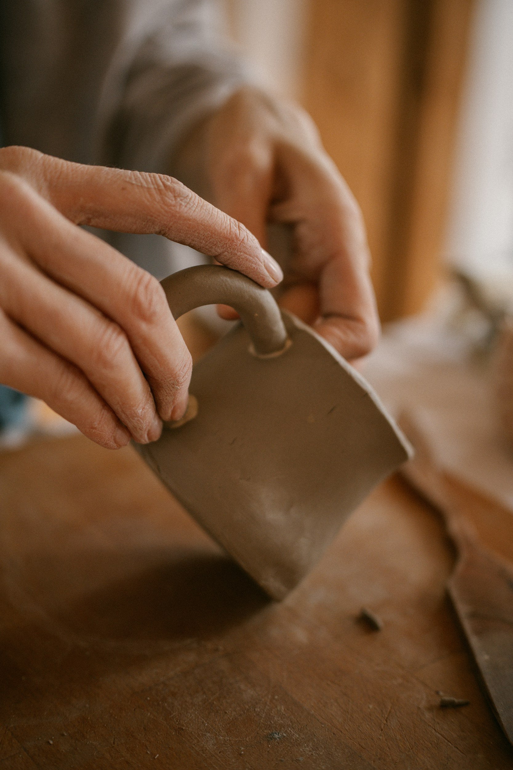 Close-up of hands holding a small pottery jug made of clay, with a wooden table surface underneath.