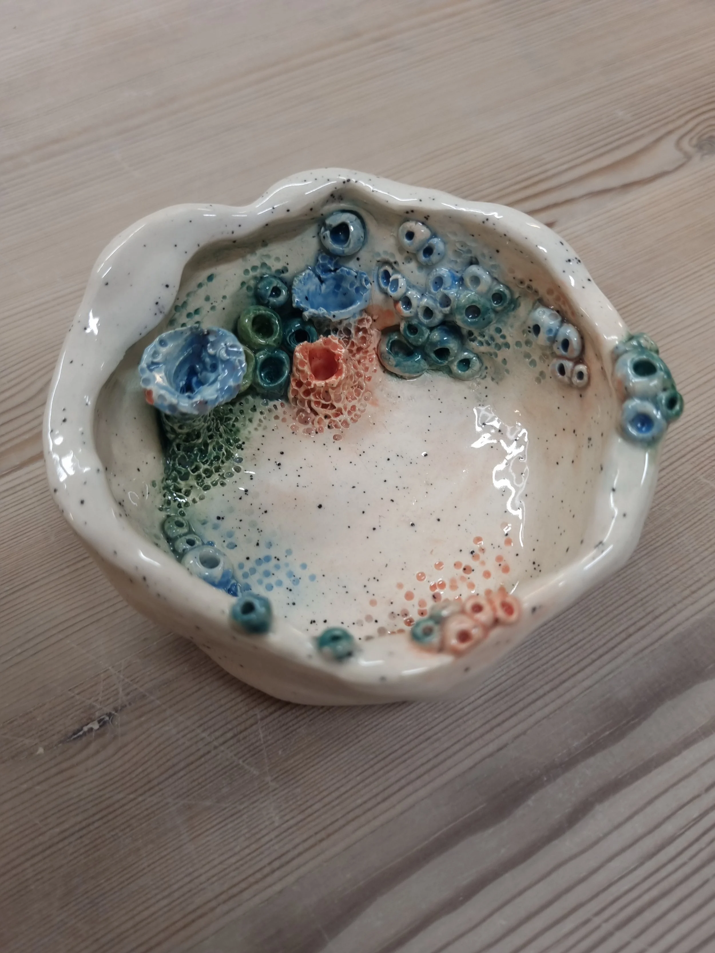 Ceramic bowl with multicolored beads resembling eyes and coral, on a wooden surface.