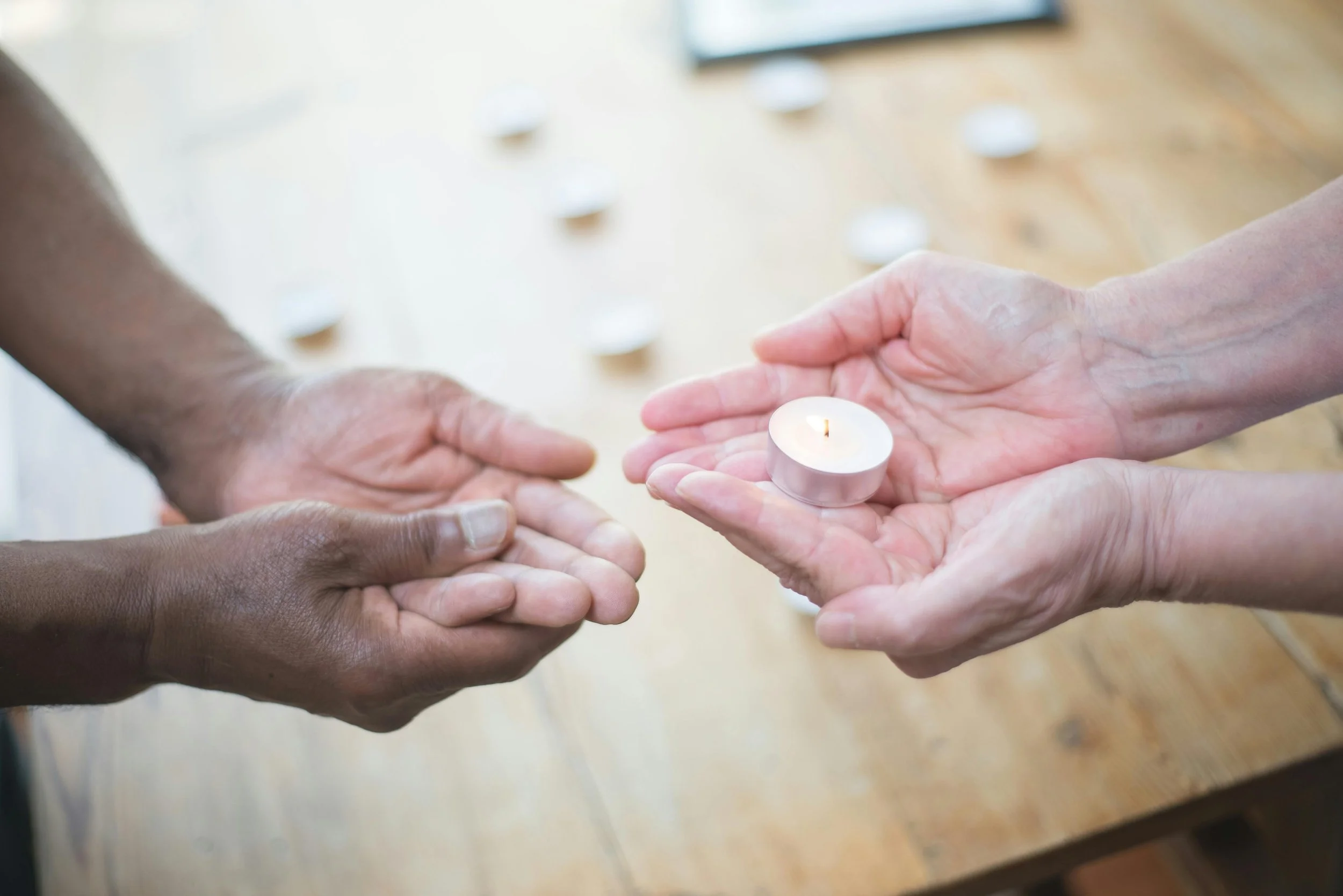 One person is handing a lit tea light candle to another person with open hands during a candle lighting ceremony.