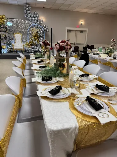 Table set for a celebration with white and gold decor, floral centerpieces, and place settings with black napkins.