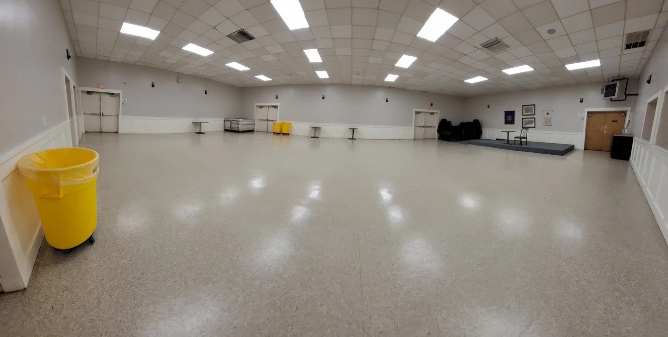 Empty event hall with a stage, chairs, and yellow trash bins.