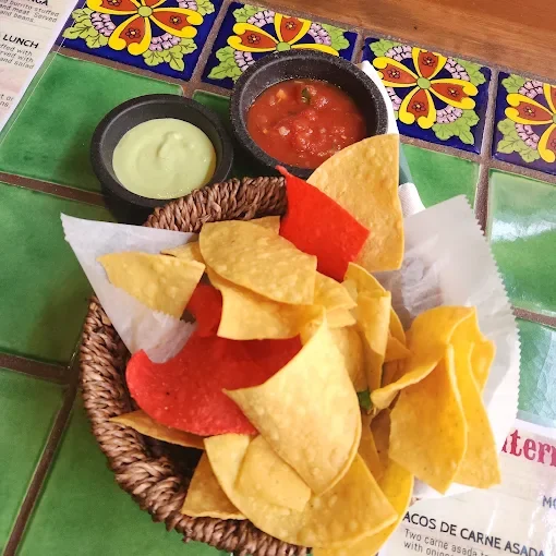 Basket of tortilla chips with salsa and guacamole on a colorful Mexican restaurant table.