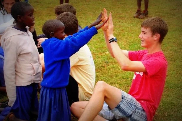 A group of children and a young man engaging in a high-five outdoors on grass.